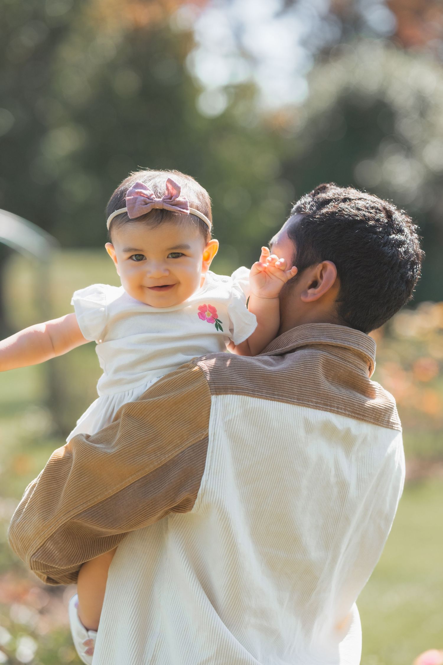 A parent and baby share a tender moment outdoors on a sunny autumn day, with soft bokeh and natural lighting.