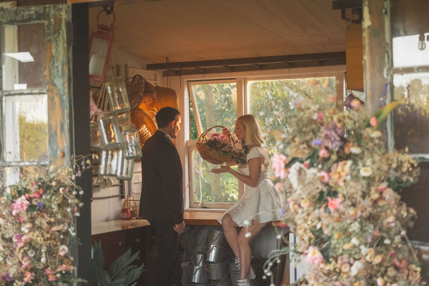 A couple exchanges a floral bouquet inside a charming flower shop surrounded by lush blooms and rustic decor.