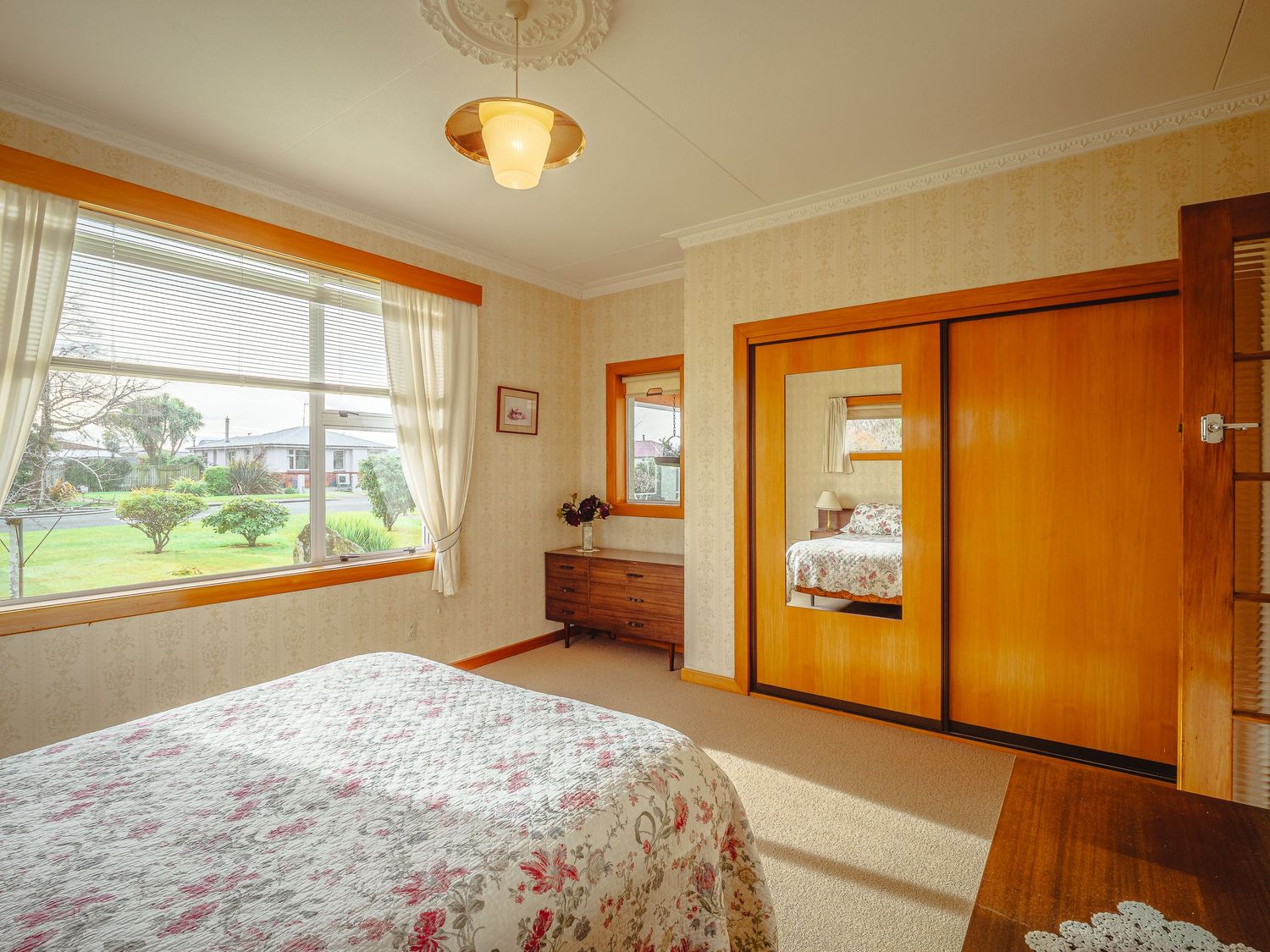 Interior view of a bright bedroom with wood trim, floral bedding, and multiple windows providing natural light.