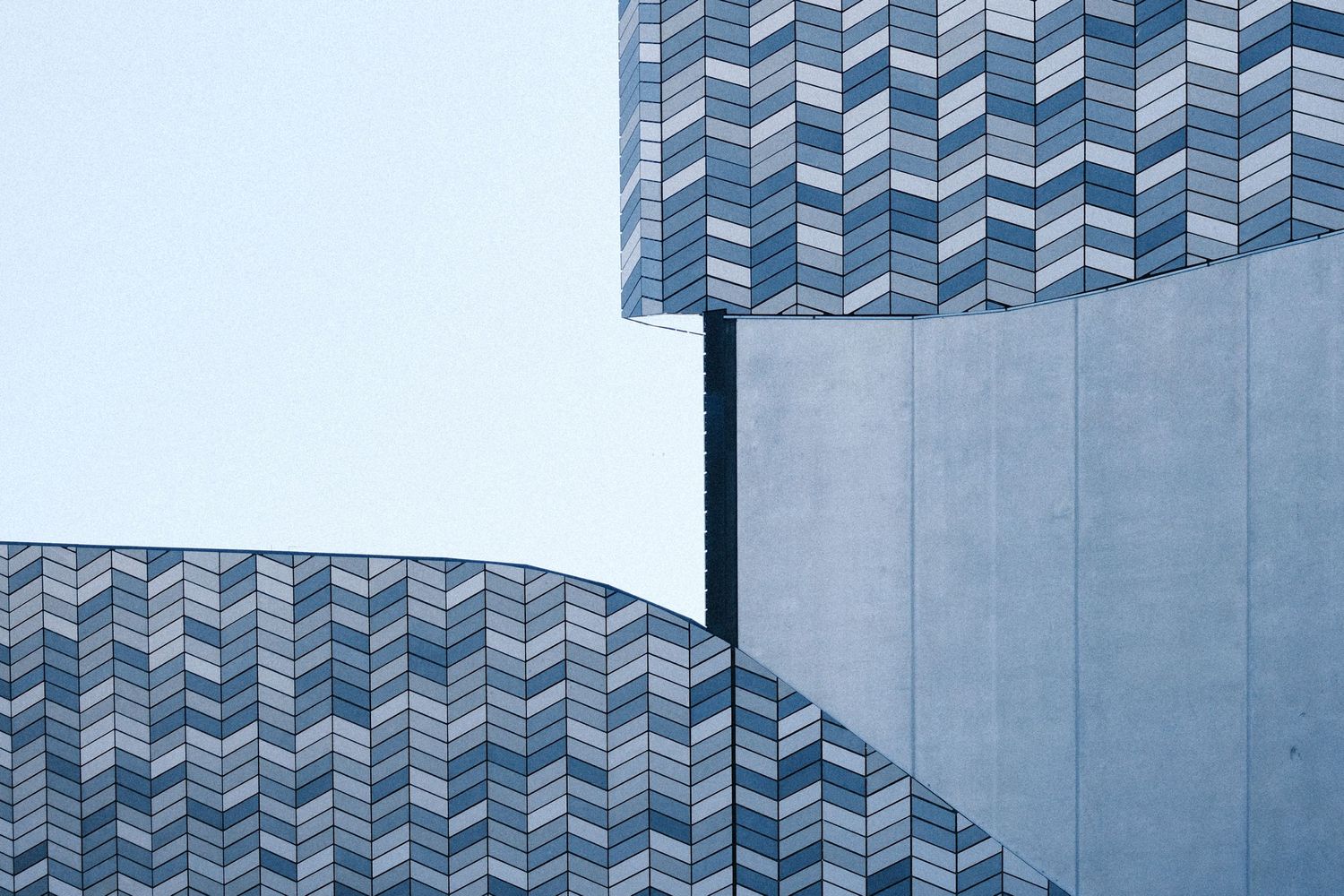 Abstract architectural facade featuring geometric chevron patterned tiles on a modern curved building against a pale sky.