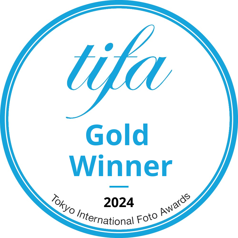 A circular blue logo badge for the Tokyo International Foto Awards 2024 Gold Winner achievement.