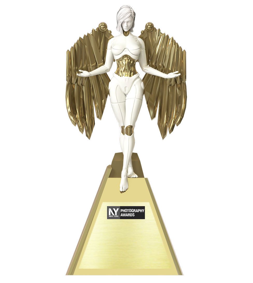 A white and gold statuette of an angel-like figure with metallic wings standing atop a triangular pedestal.