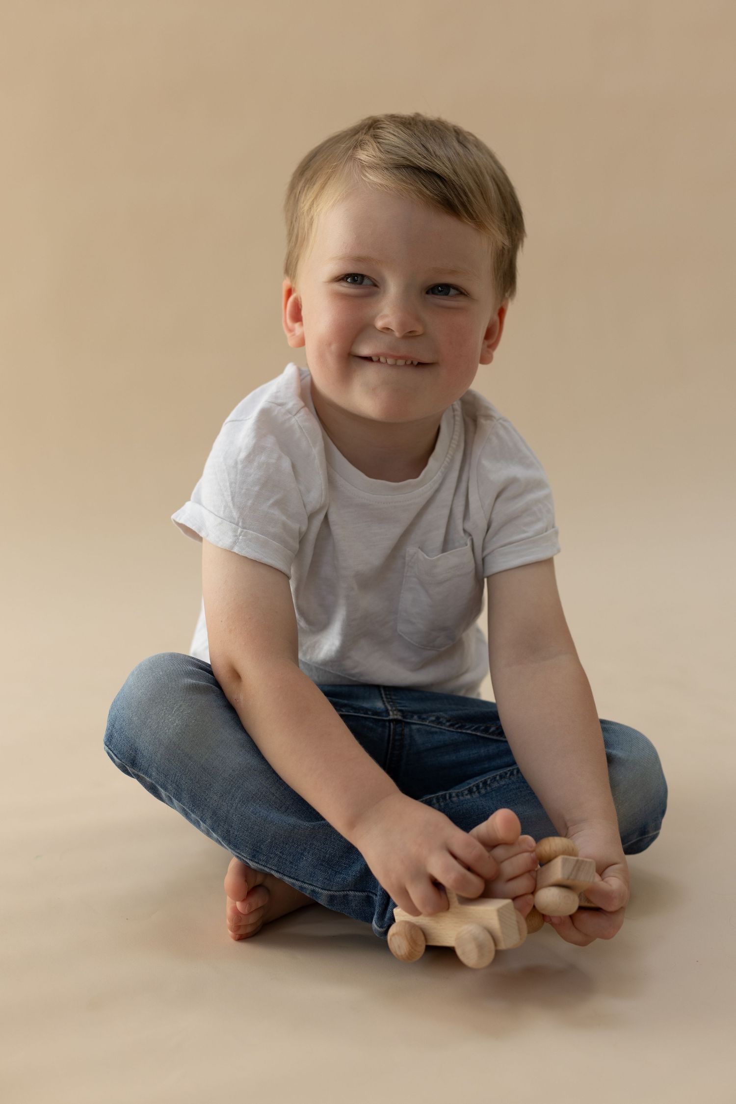 A child in blue jeans and white t-shirt sits on a beige floor in a series of progressive poses.