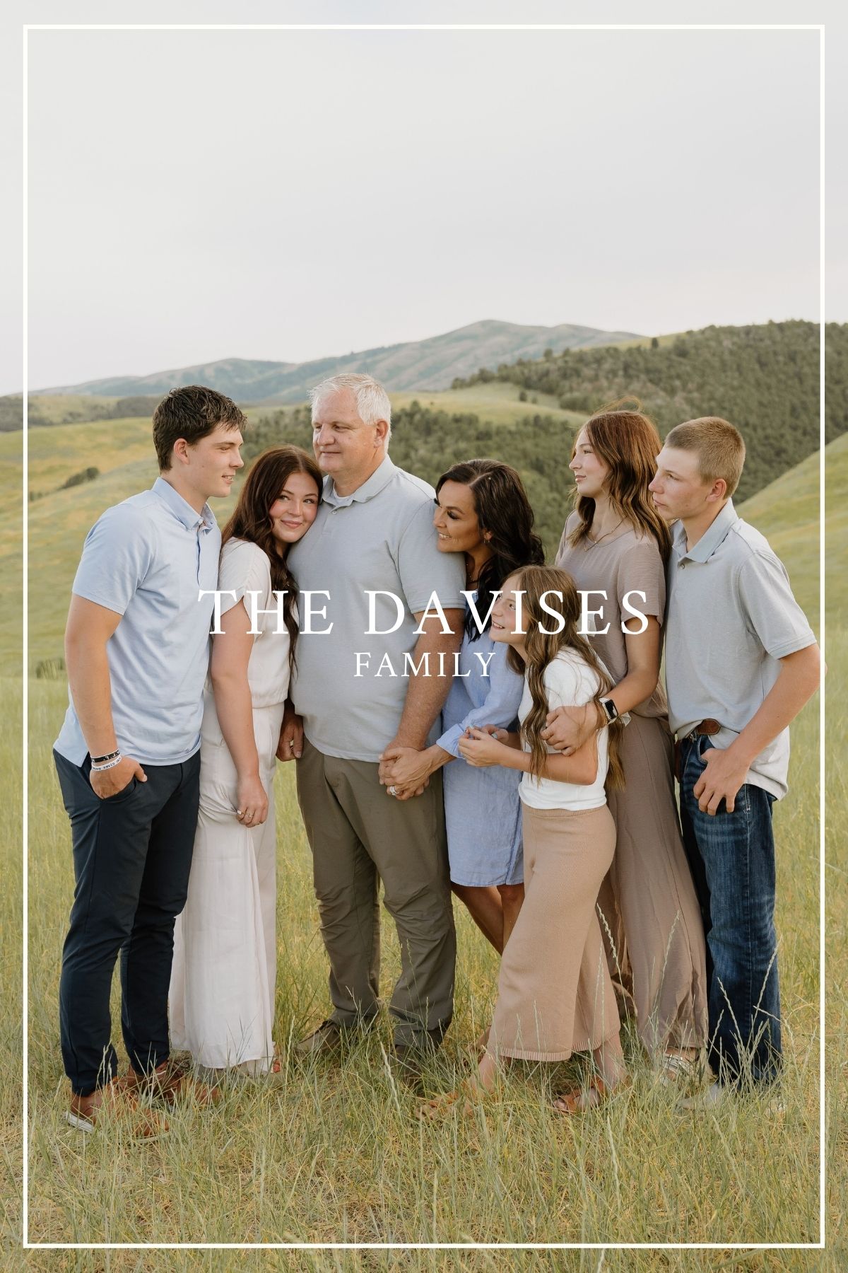 A family stands together in casual attire against a scenic mountain backdrop for their portrait session.