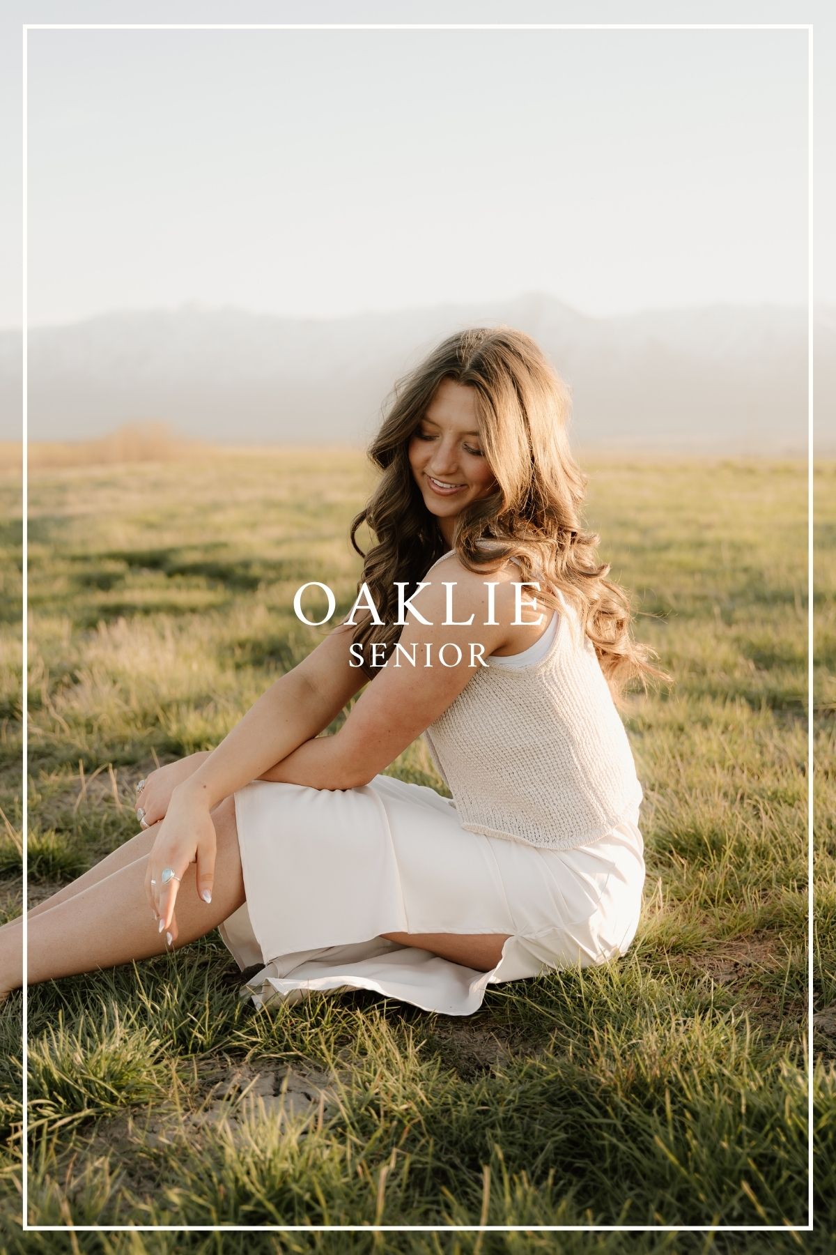 Senior portrait photo of someone in a white dress sitting in a sunlit grassy field at golden hour.