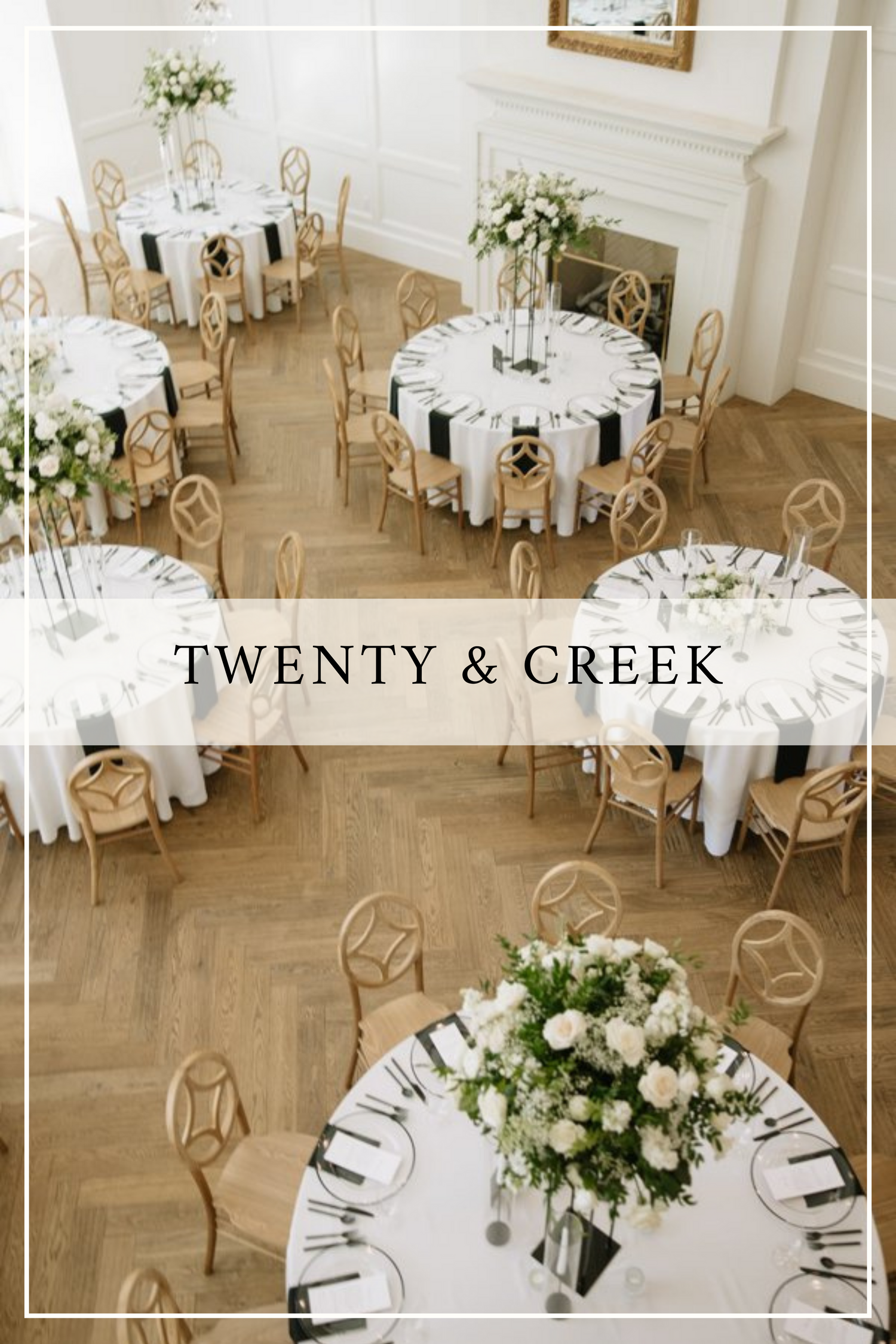 Elegant wedding reception venue with white round tables, gold chairs and white floral centerpieces on herringbone wood floors.