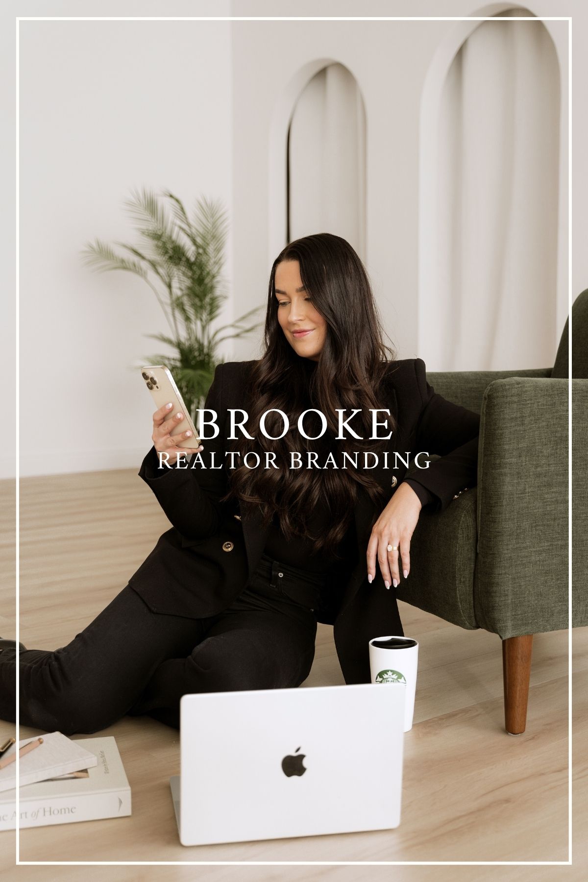 Real estate professional in black outfit sits comfortably with laptop and phone in minimalist room with arched doorways.