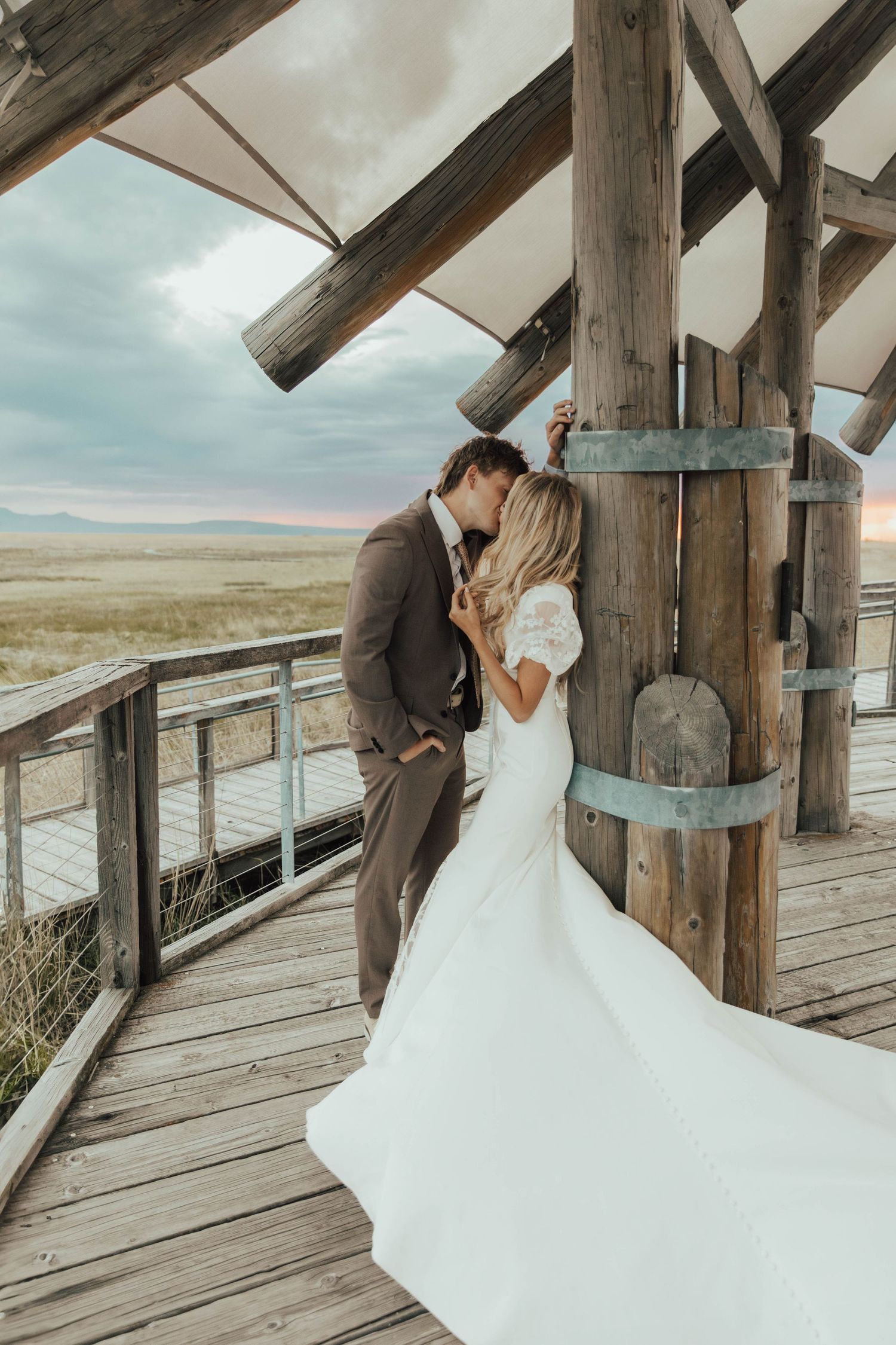 A romantic wedding moment on a rustic wooden deck overlooking vast open prairie landscapes.