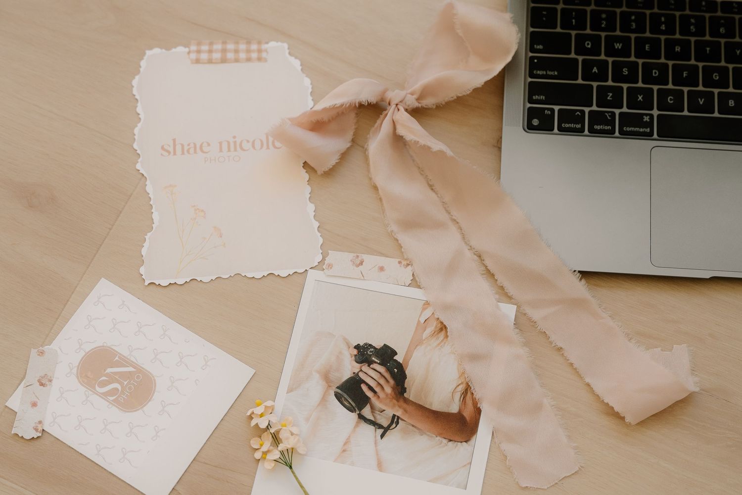 Wedding stationery with pale pink bow ribbon laid next to a silver laptop keyboard and floral elements.