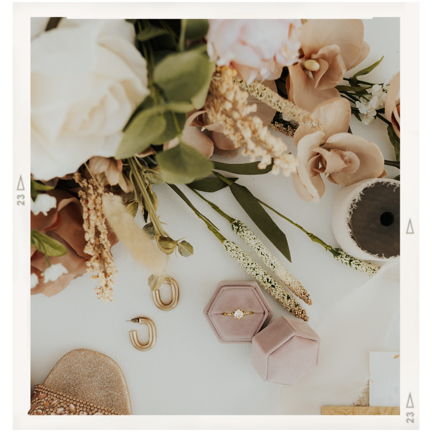 Wedding accessories including roses, jewelry, and a pink hexagonal ring box arranged on a light surface.
