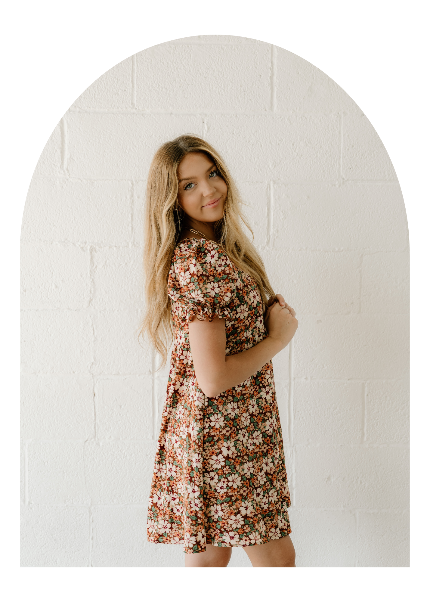 Woman models brown floral midi dress with puff sleeves against white backdrop.