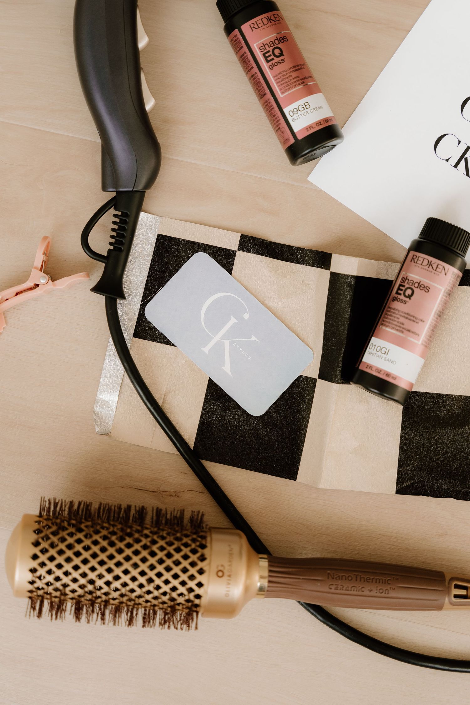 Hair styling products and tools including round brush, hair dryer and beauty products arranged on beige surface.