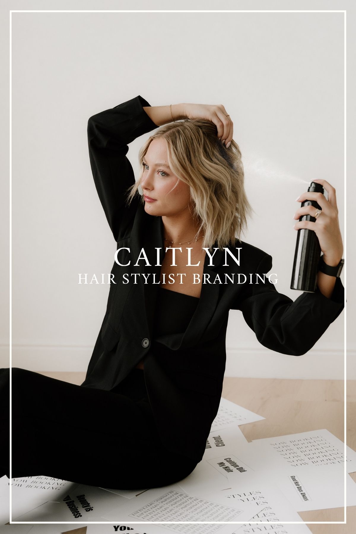 A hairstylist wearing black holds a styling product while posing against a neutral background in a branding photoshoot.