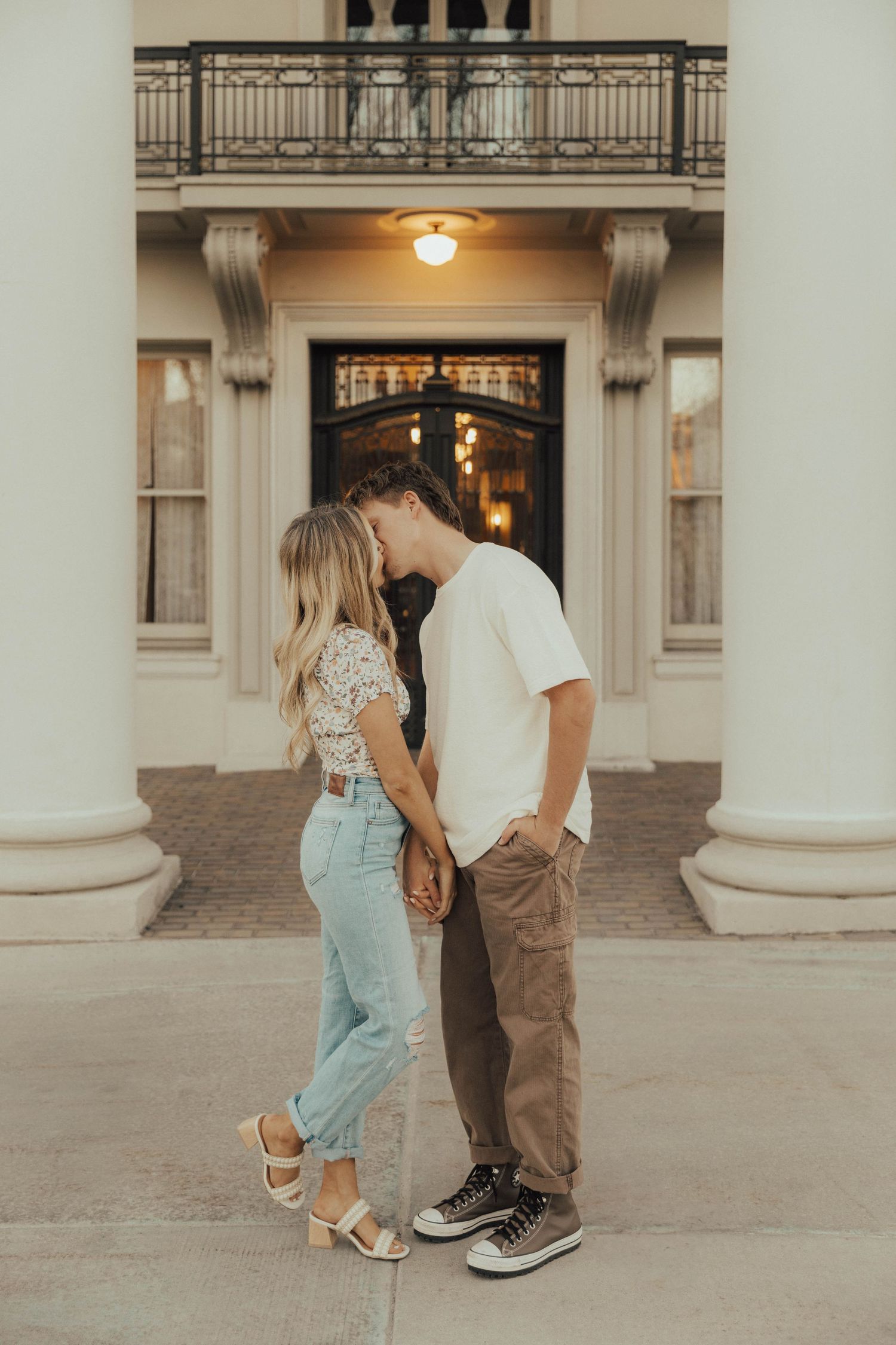 Romantic couple shares tender moment between elegant columns at sunset with warm glowing light behind them.