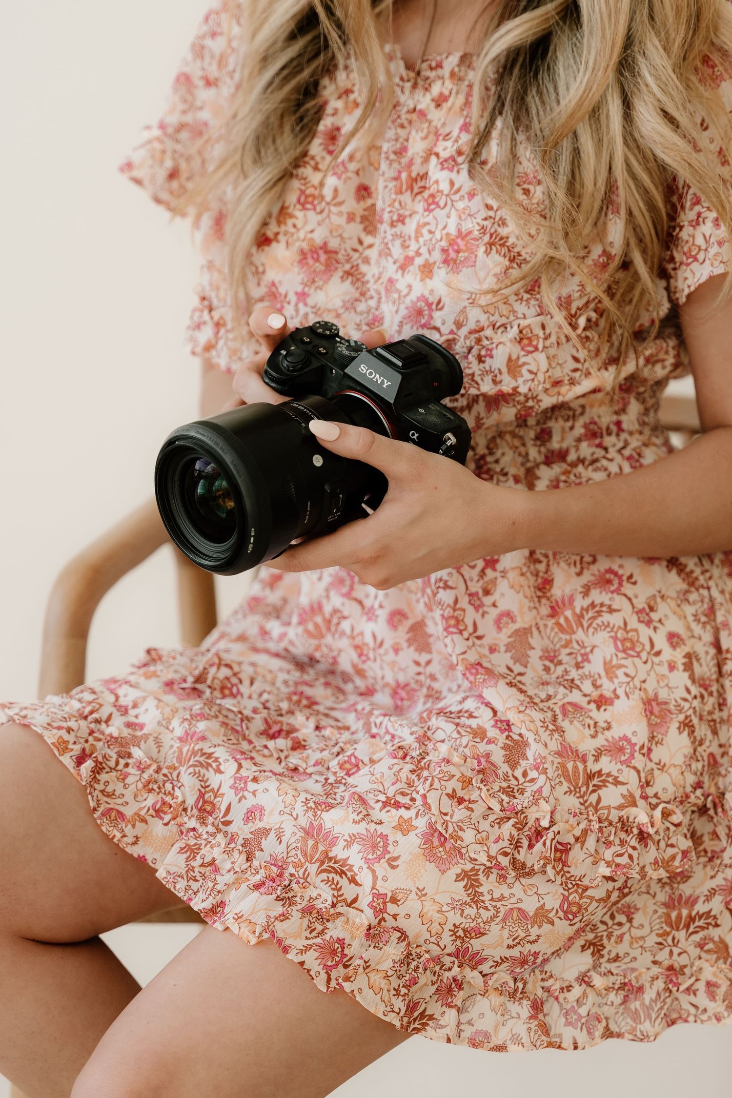 Person wearing floral pink dress holding professional camera while sitting, with focus on camera equipment and floral pattern.