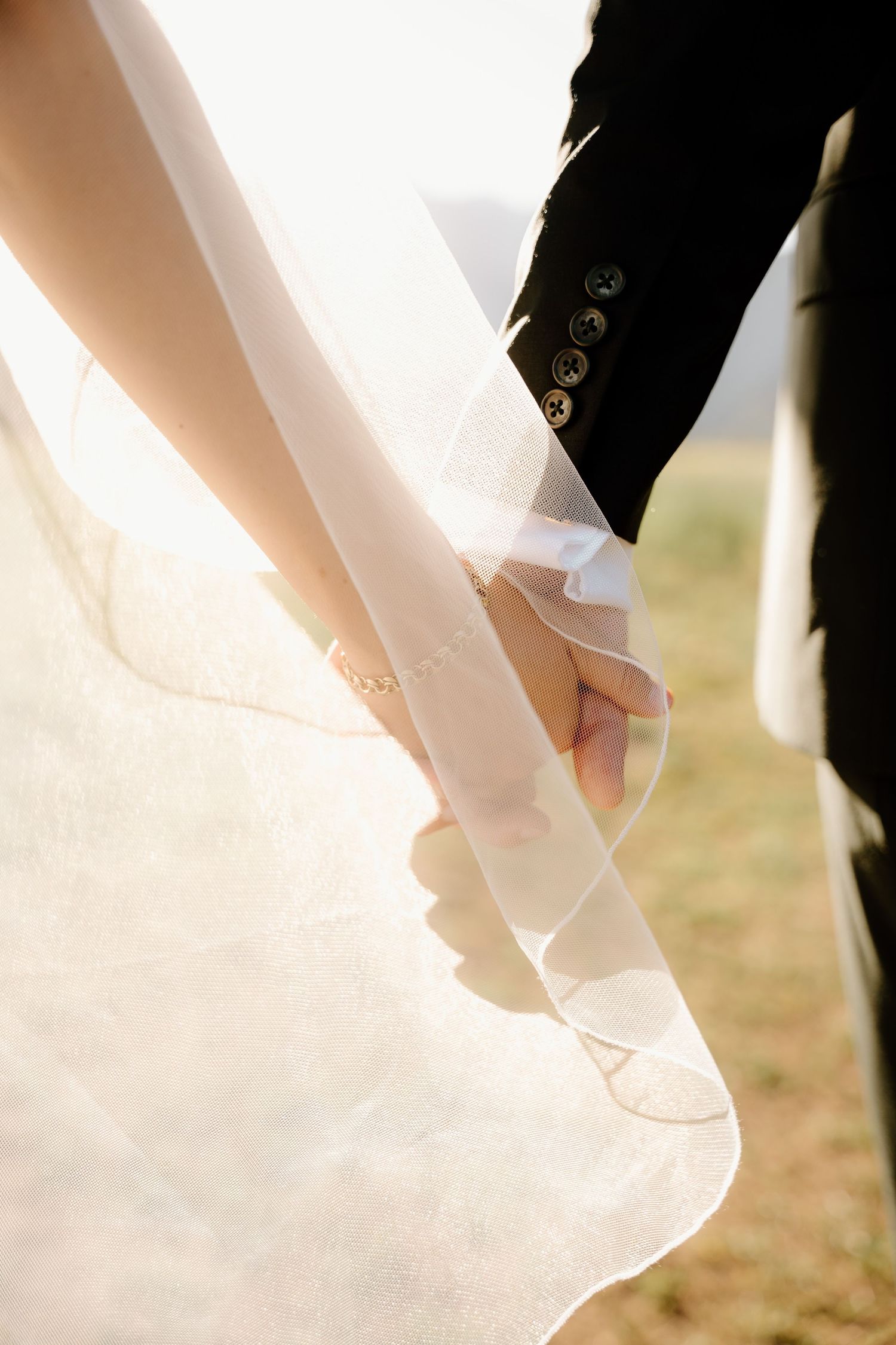 Close-up detail of wedding couple holding hands with white dress fabric and black suit sleeve.
