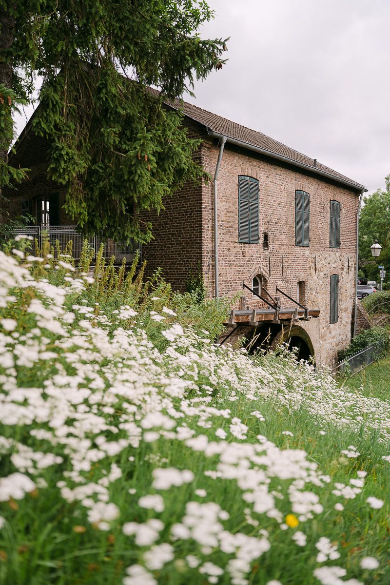Die Welsche Mühle in Aachen Haaren liegt eingebettet zwischen grünen Bäumen und sanften Hügeln auf dem Land.
