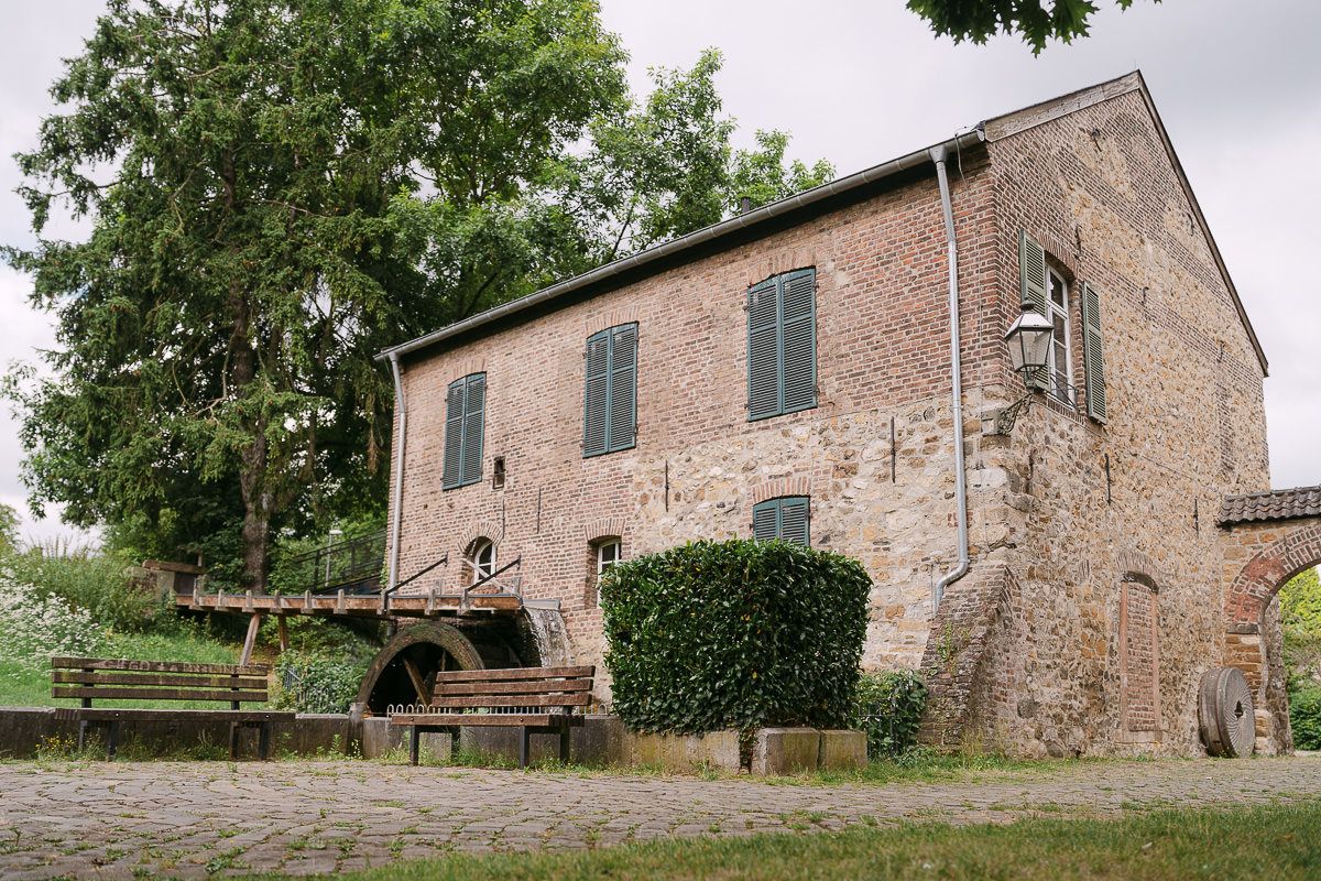 Die Welsche Mühle in Aachen Haaren liegt eingebettet zwischen grünen Bäumen und sanften Hügeln auf dem Land.