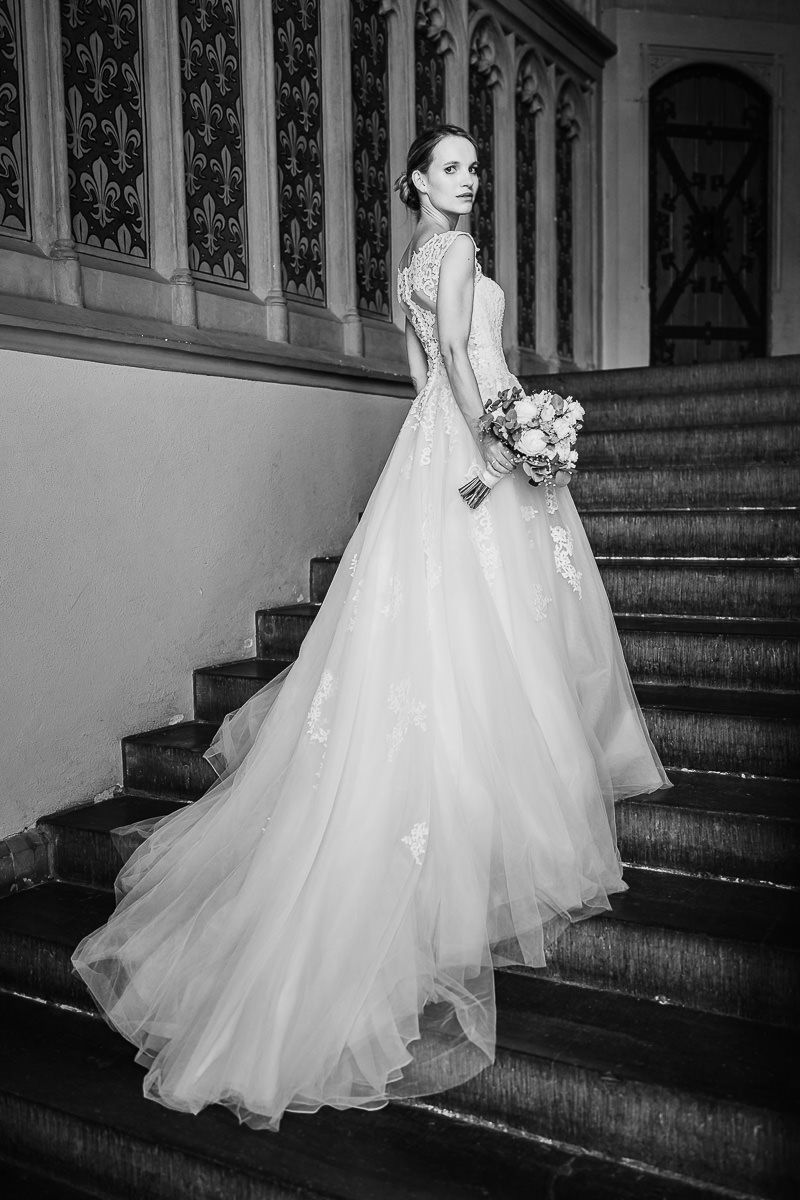 Editorial-Portrait einer Braut in einem fließenden weißen Tüllhochzeitskleid, die auf der Treppe im Aachener Rathaus steht.