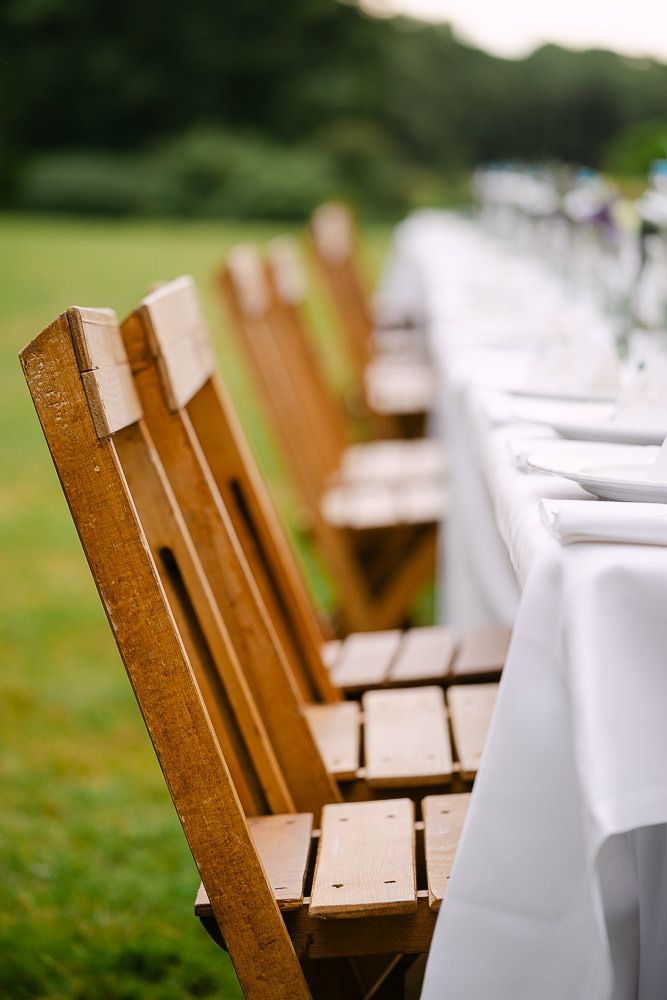 Wooden chairs arranged at the wedding reception table in the garden of Kasteel Aerwinkel.