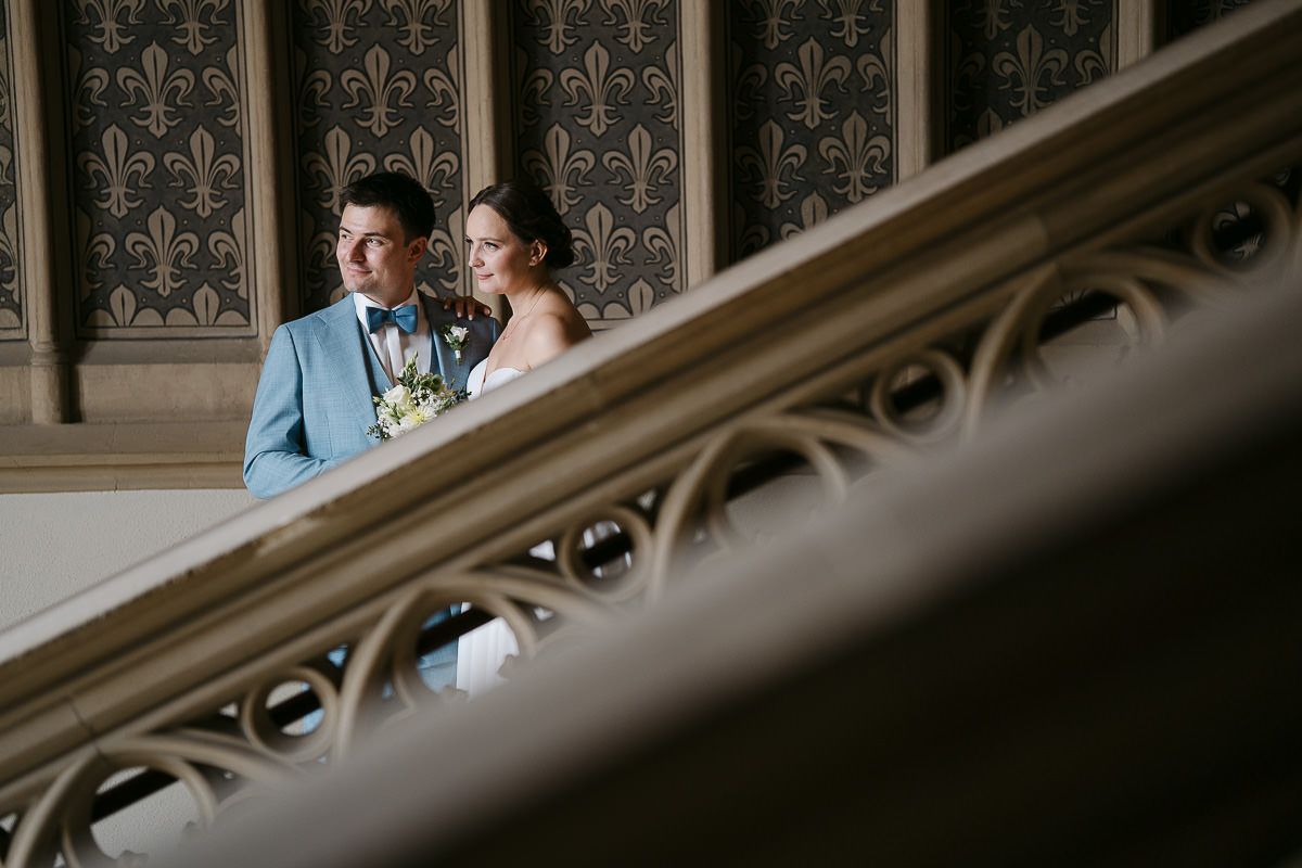 Couple embracing in front of an ornate vintage wallpapered wall during elegant indoor photo session.