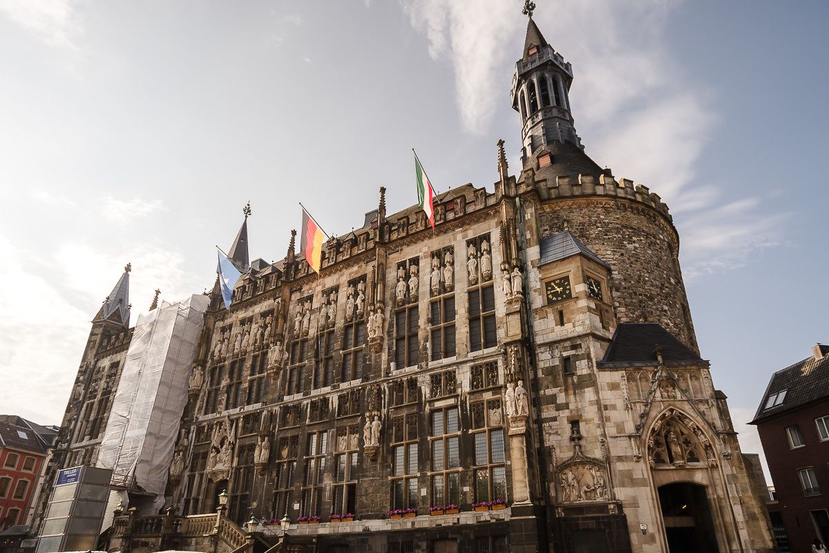 Die gotische Architektur des historischen Aachener Rathauses mit seiner reich verzierten Fassade und dem Turm vor einem bewölkten Himmel in