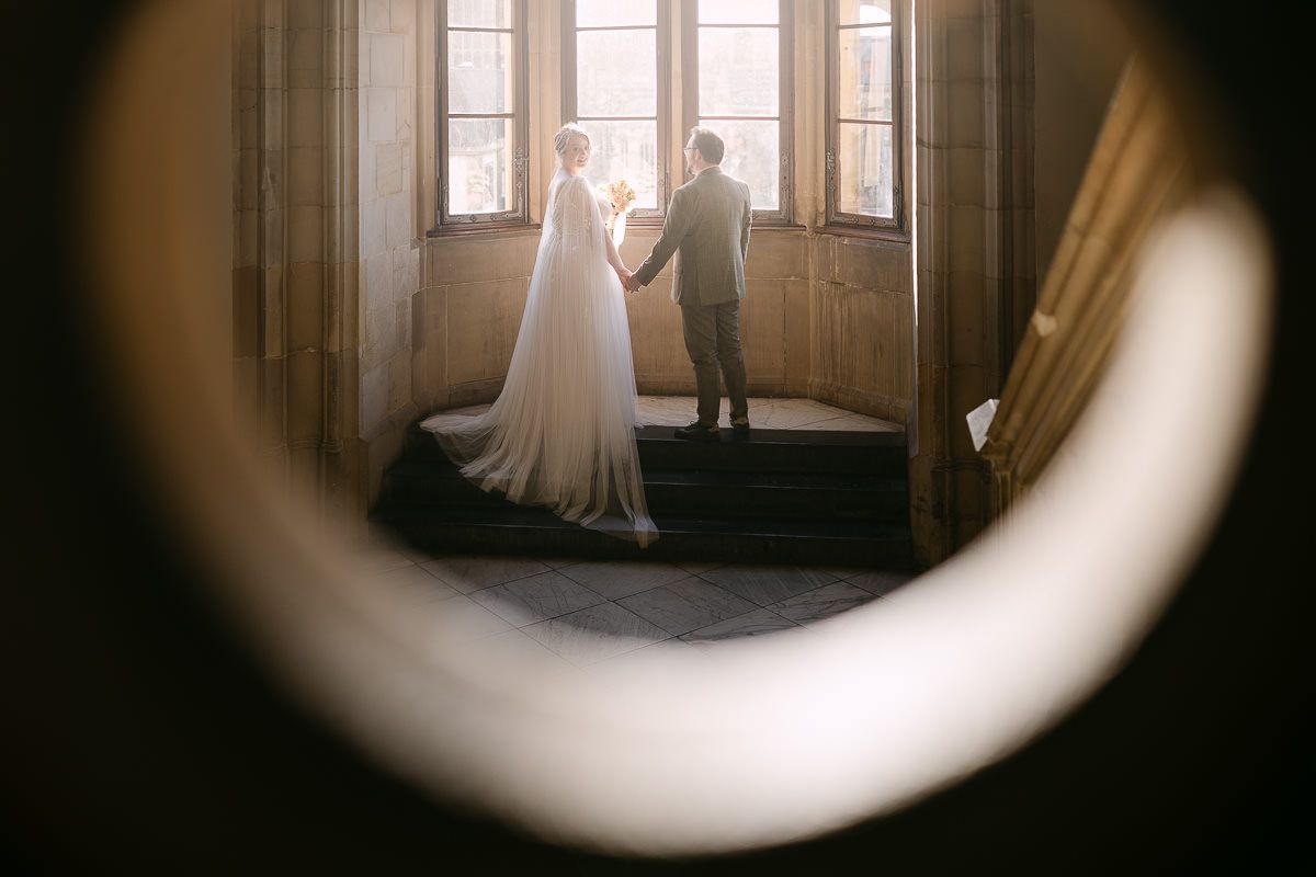 Ein Brautpaar steht als Silhouette vor einem hellen Fenster im schwach beleuchteten Inneren des historischen Rathauses Aachen.