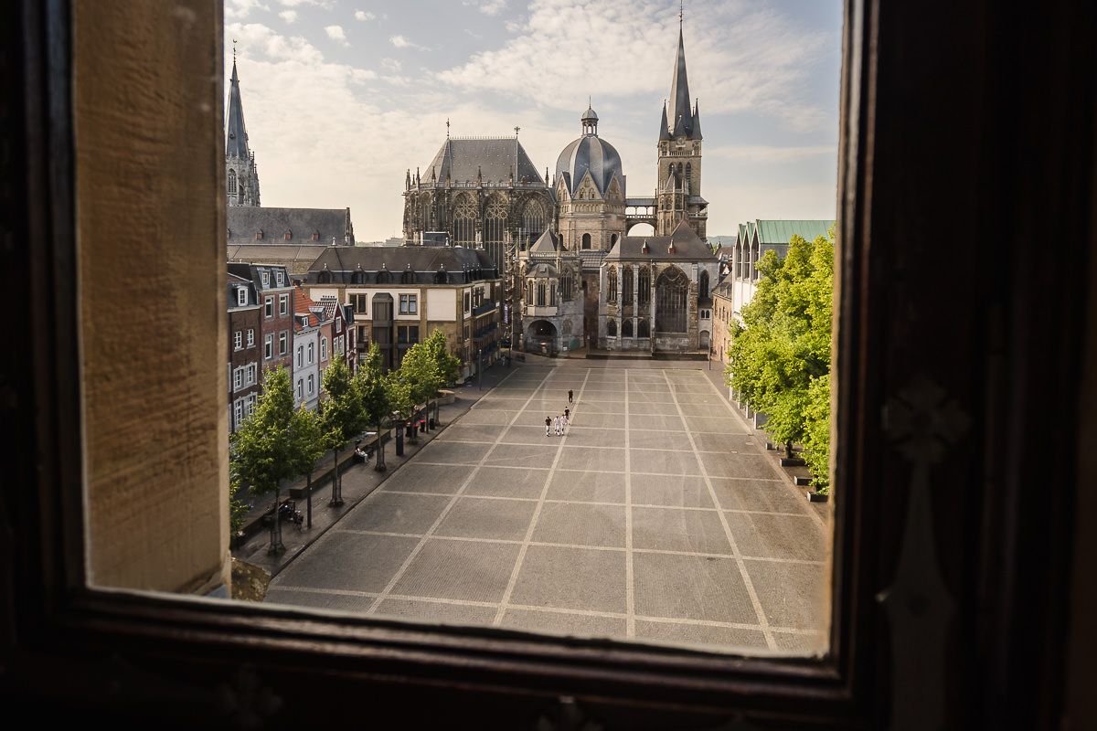 Architektonische Ansicht des Aachener Doms und historischer Gebäude am Katschhof durch ein Fenster des Aachener Rathauses.