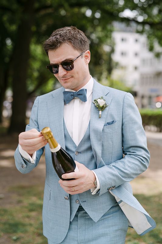 Groom opening champagne during elegant park picnic.