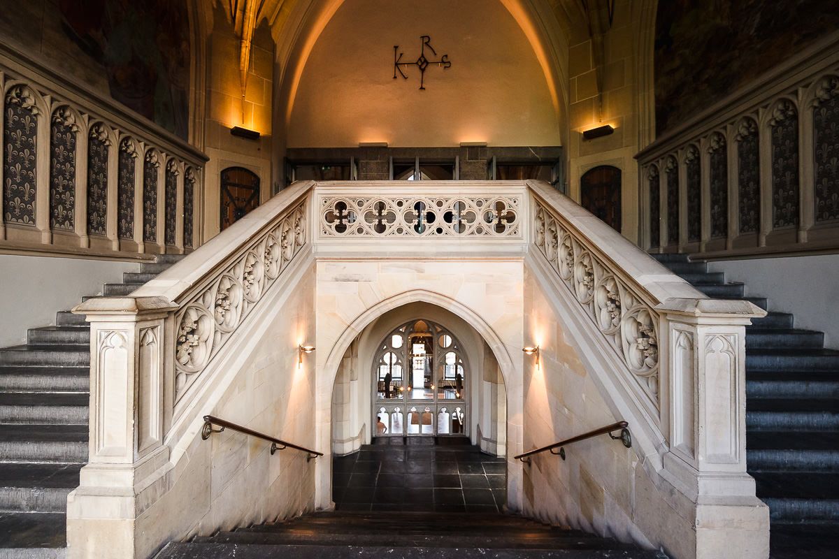 Elegante Marmortreppe mit kunstvollem Geländer und gewölbter Decke im Inneren eines historischen Gebäudes, beleuchtet von Wandleuchten.