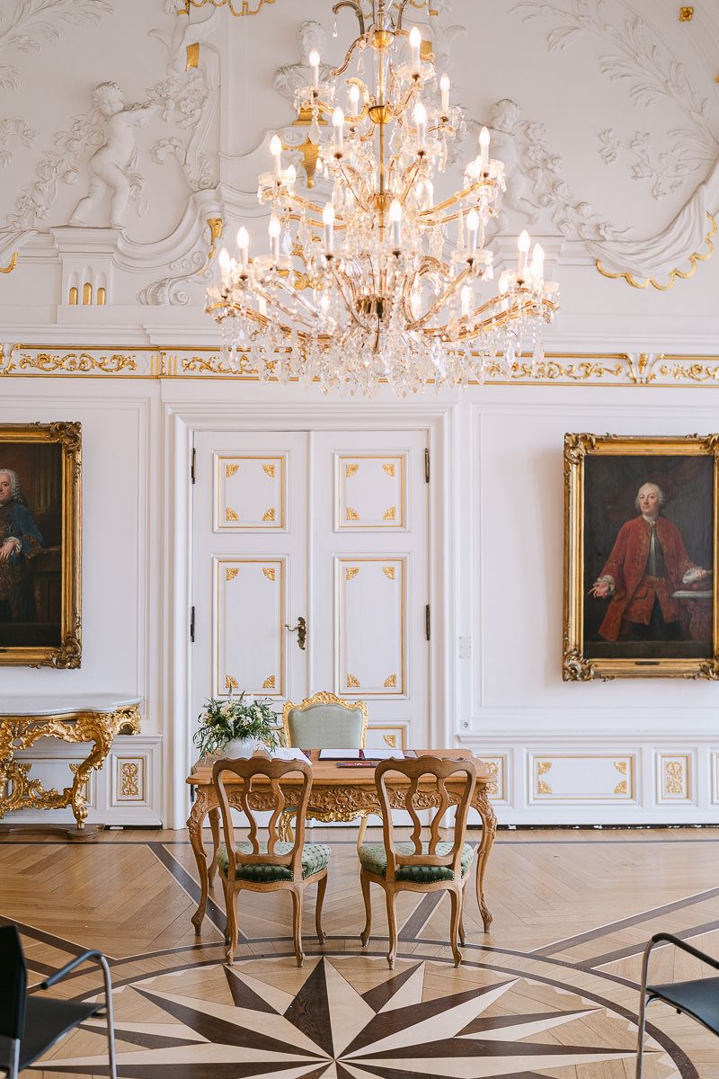Elegantes, weißes Interieur im Barockstil mit kunstvollen Kronleuchtern, vergoldeten Details, antiken Möbeln und geometrischem Bodenmuster .