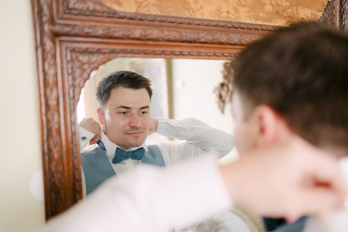 Groom adjusts bow tie in mirror before civil ceremony.