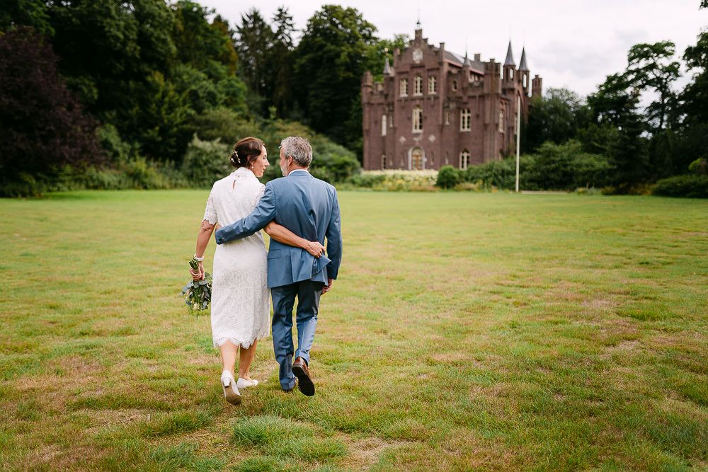 Bride and groom strolling together with castle view in the background at Kasteel Aerwinkel.