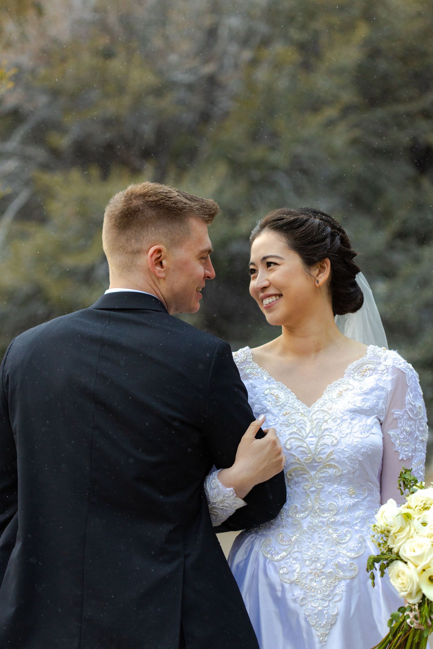 A newlywed couple shares intimate laughs in their wedding attire while posing for outdoor portraits.