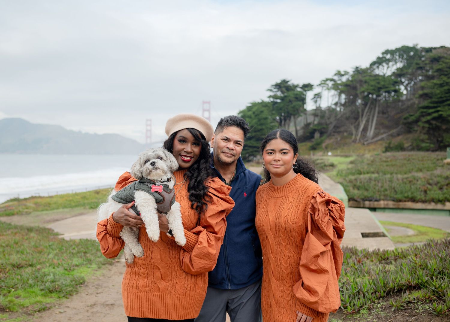 Family posing with their dog on a cloudy coastal path wearing matching orange sweaters.