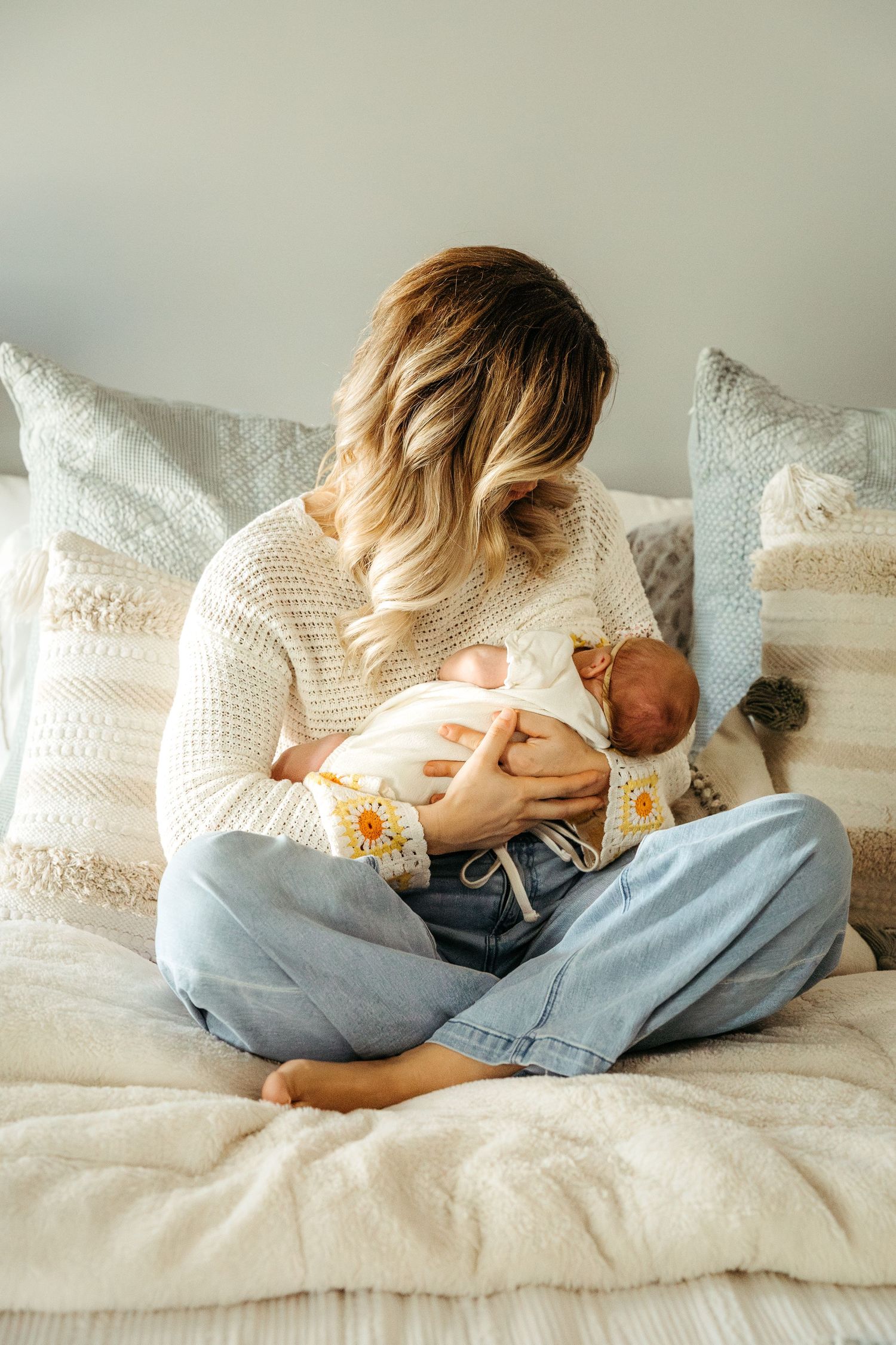 A series of photos showing a parent cradling and nursing a newborn baby on a cozy white bed with pillows.