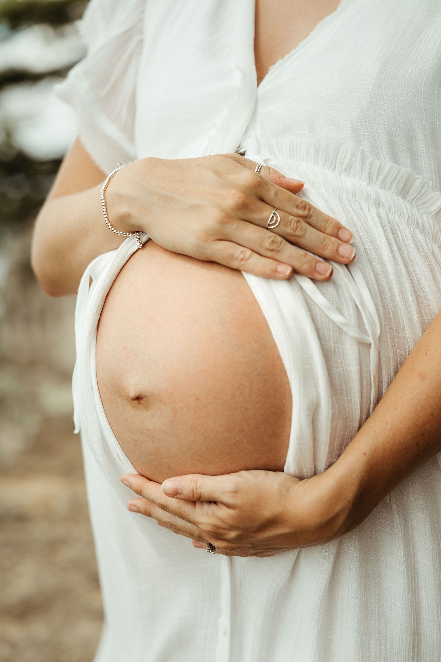 Close-up shots of pregnant belly in white flowing dress showing different angles against natural backdrop.