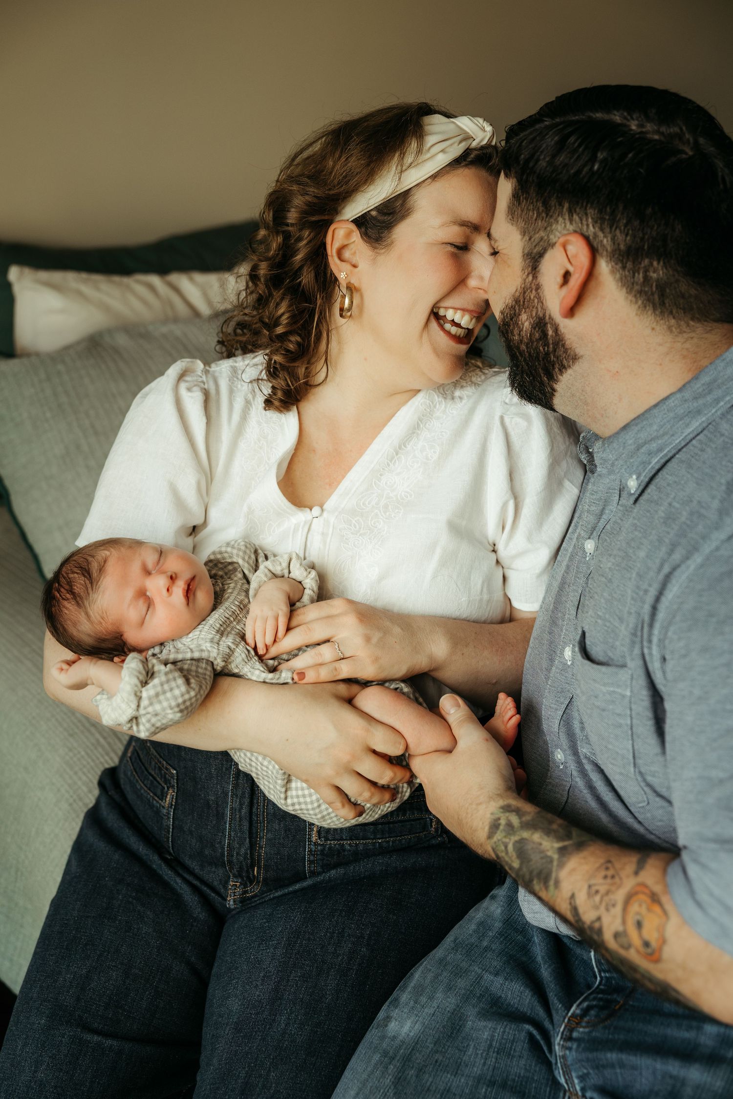 A couple shares an intimate moment while holding their newborn baby on a couch at home.