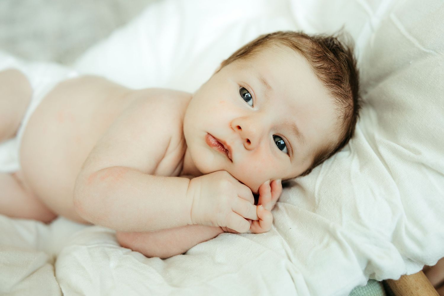 Baby lying on white bedding looking upward with soft, gentle expression.