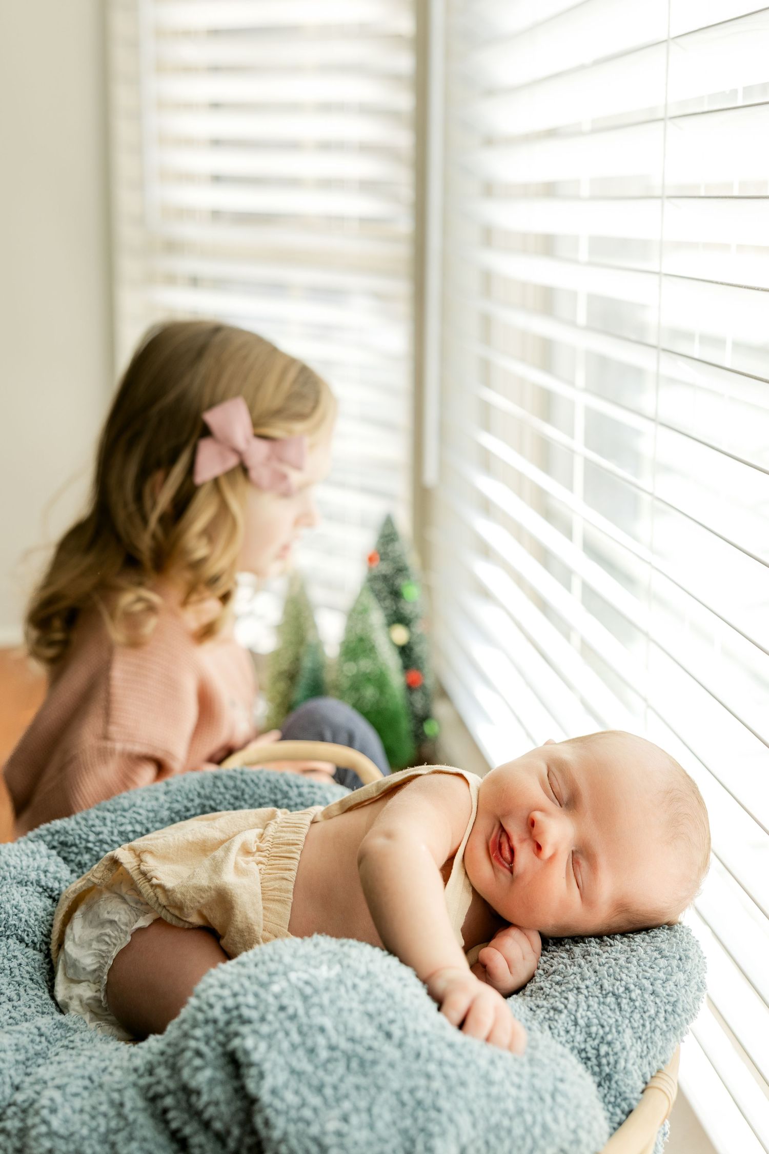 A sleeping baby lies peacefully on a soft blue blanket near a window with natural light streaming in.