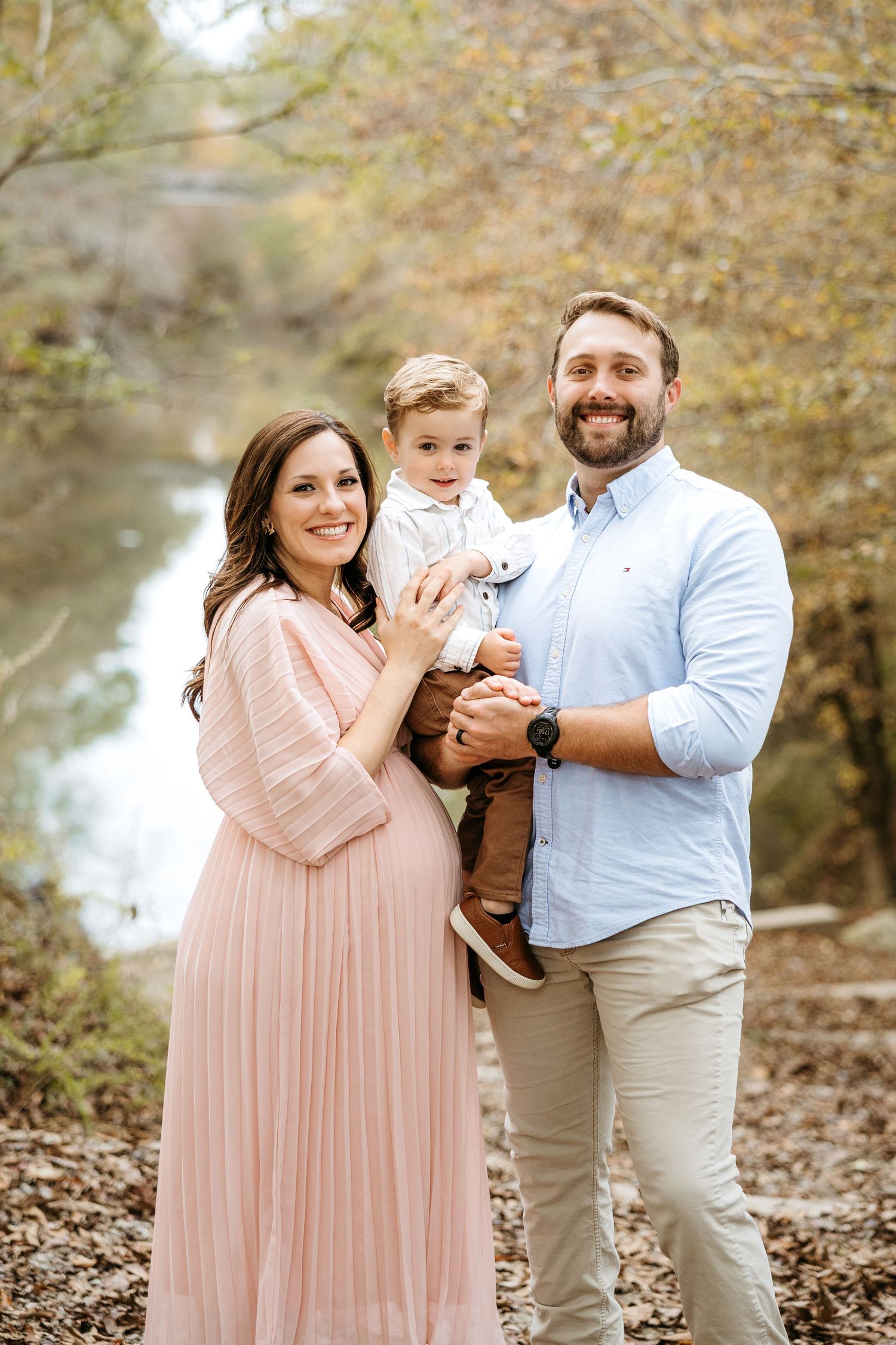 A family in coordinated pink and beige outfits poses together during an autumn photoshoot with fallen leaves.