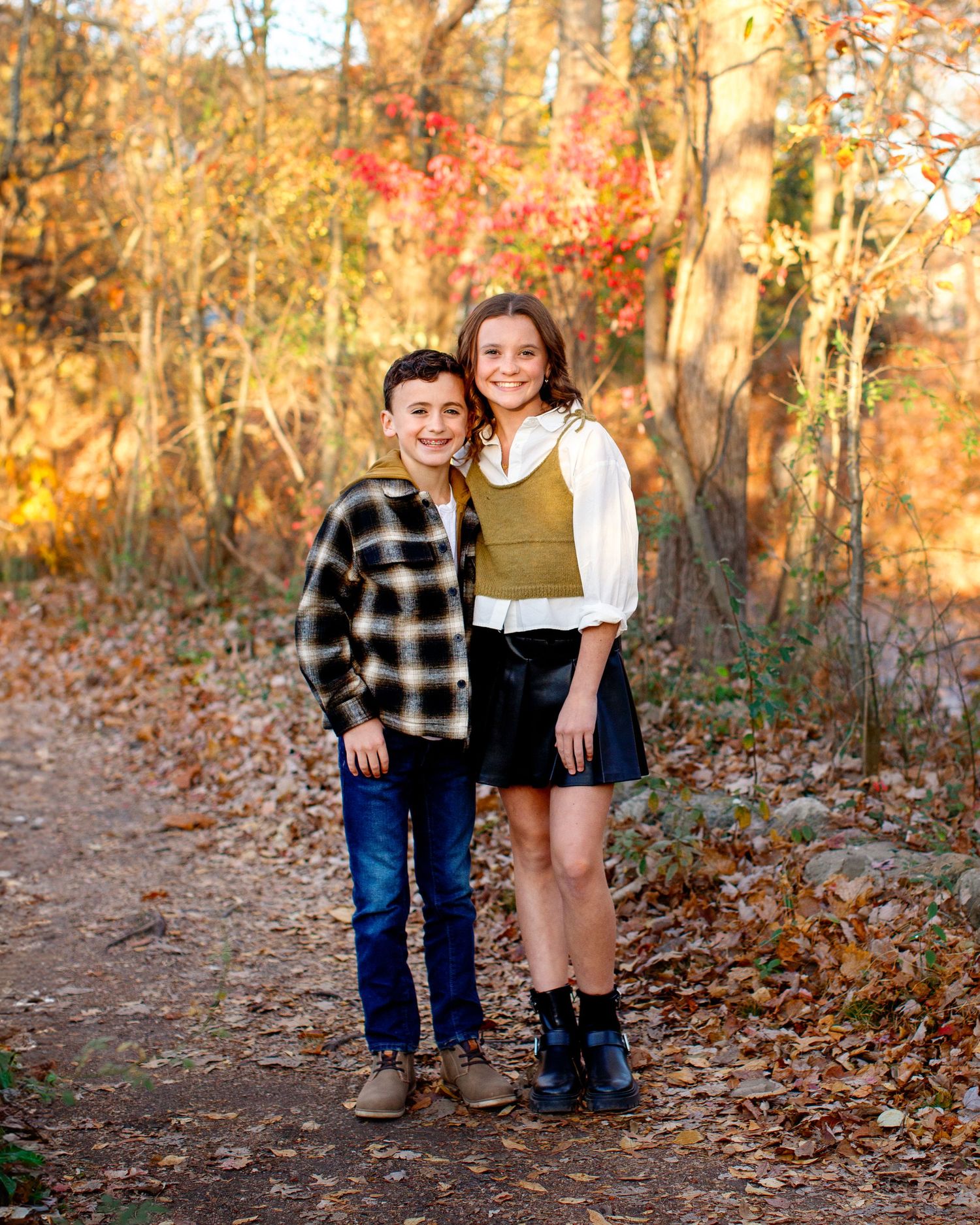 Bergen County Photographer capturing sibling photoshoot outside.  Brother and sister in a park with fall foliage around them.