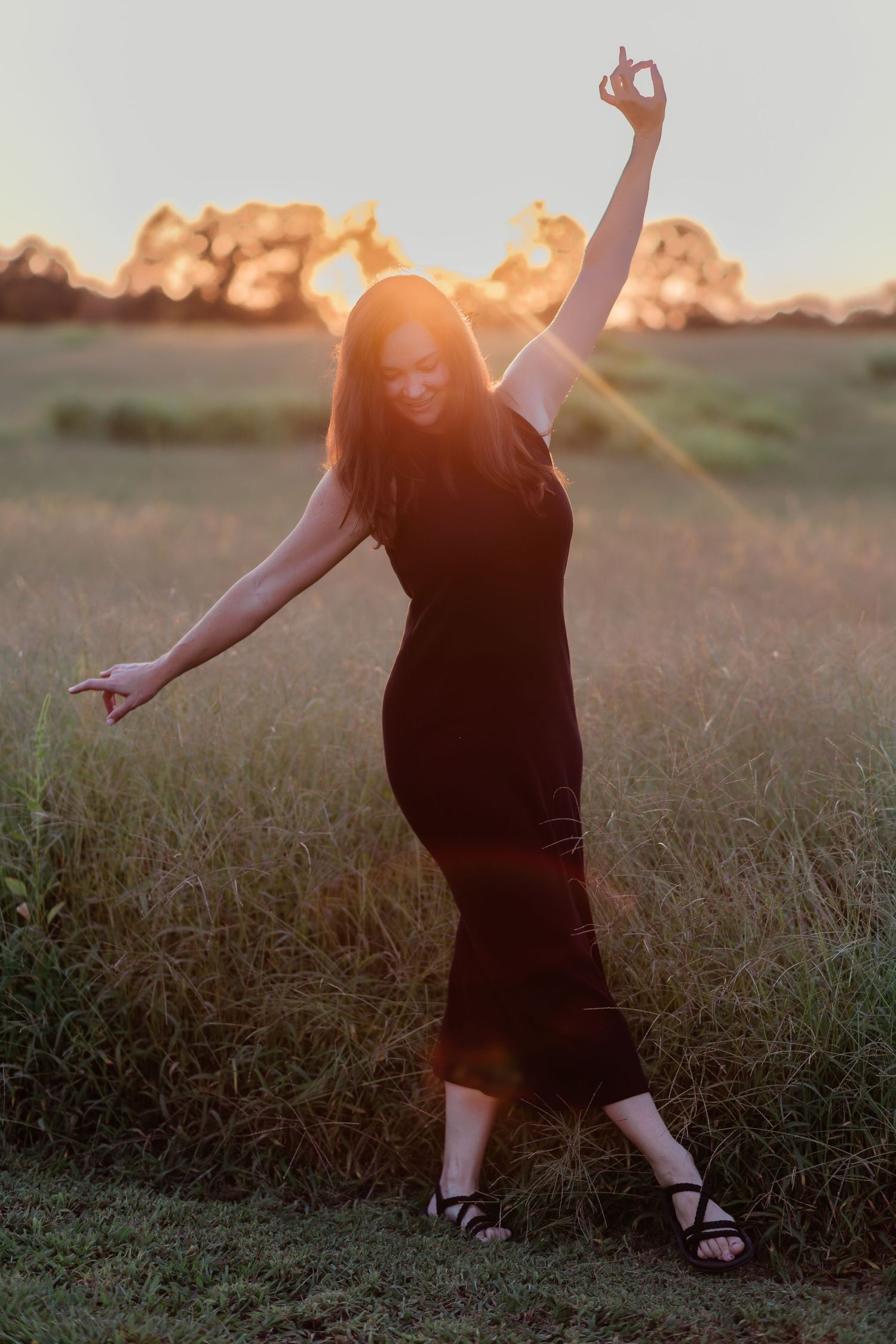 A silhouetted figure dances joyfully in a black dress against a sunset sky.