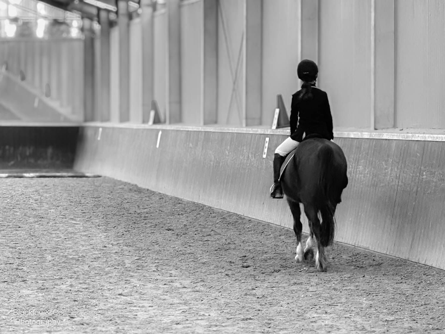 Black and white photo of a rider on horseback practicing dressage in an indoor equestrian arena.