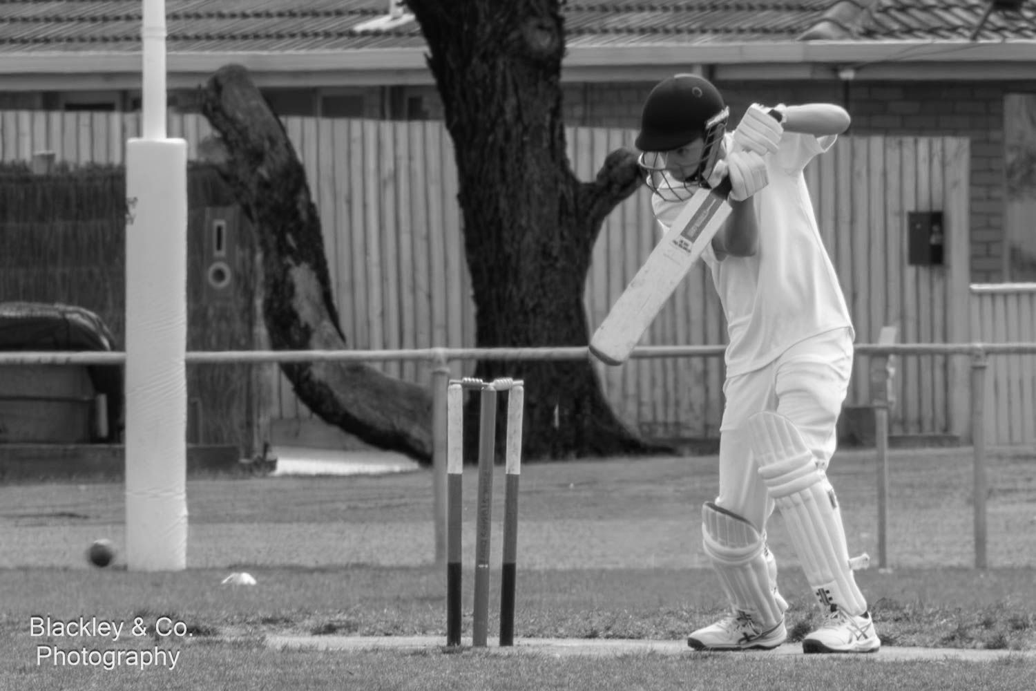 Black and white photo of a cricket batsman in defensive stance near the wickets during a match.