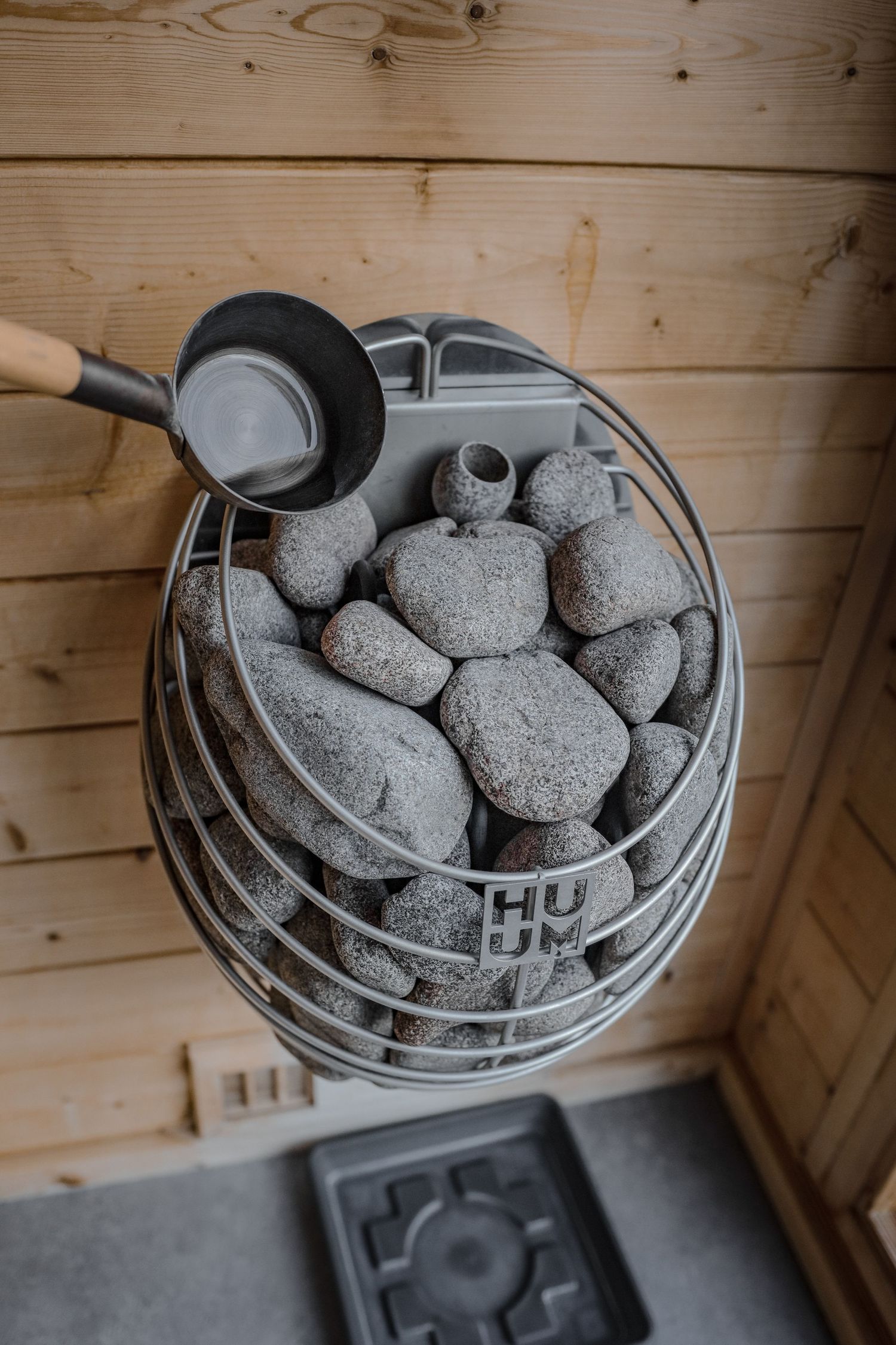 HUUM sauna heater filled with stones and a ladle in a wooden sauna.