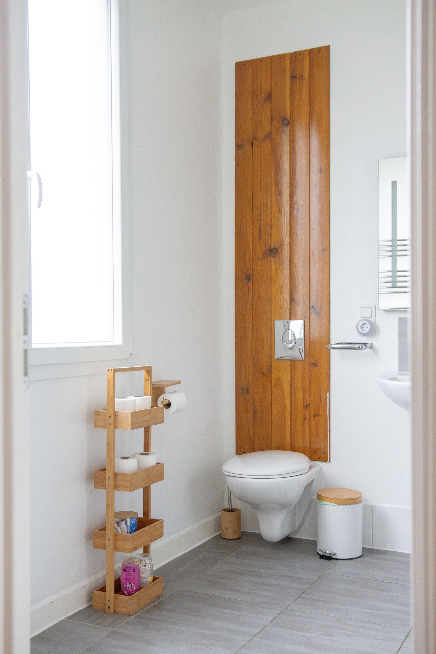 Clean white bathroom with wooden accents, wall-mounted toilet, and bamboo storage shelf.