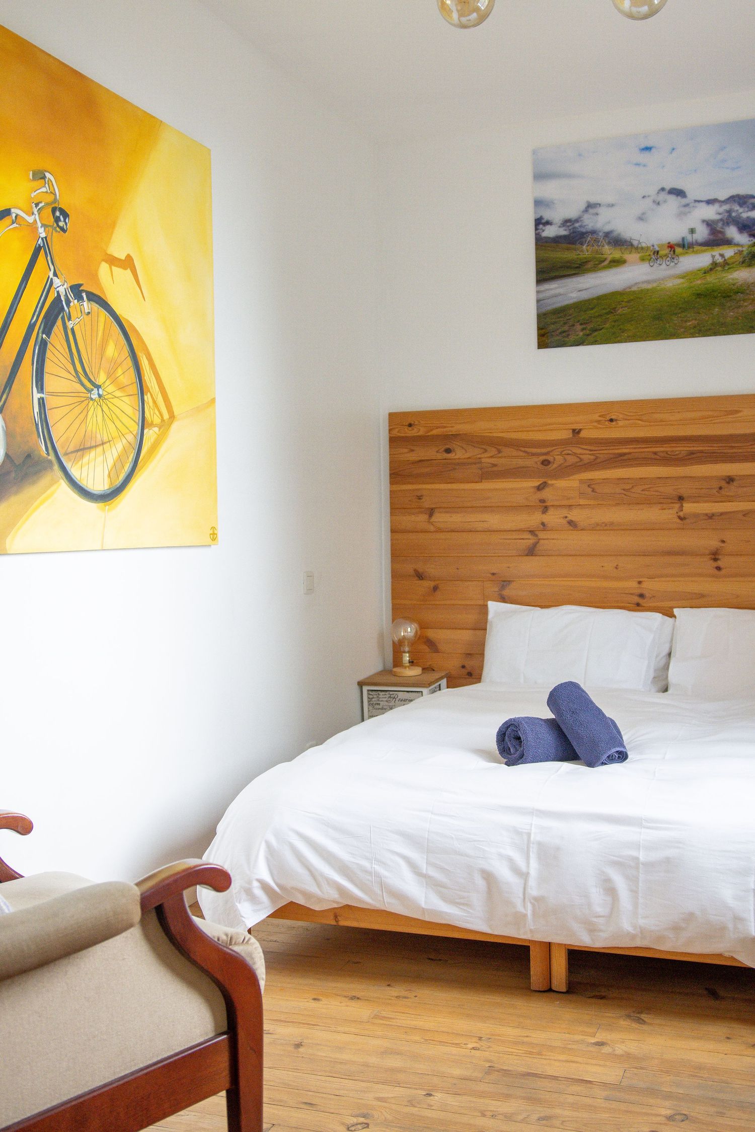 Cozy bedroom with wooden headboard, white bedding, and a bicycle painting on the wall.