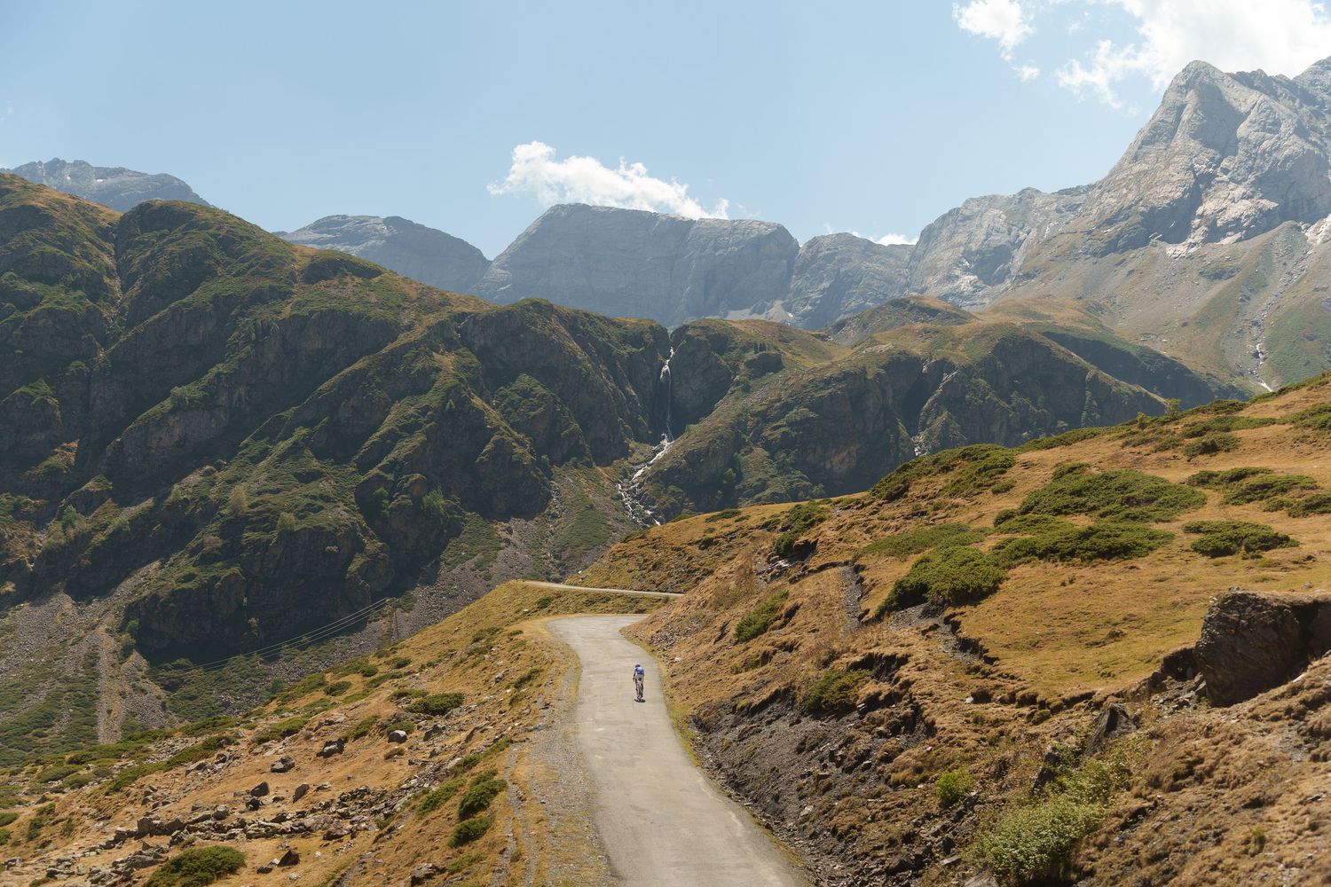 Winding mountain road through dramatic Pyrenees landscape under partly cloudy sky.