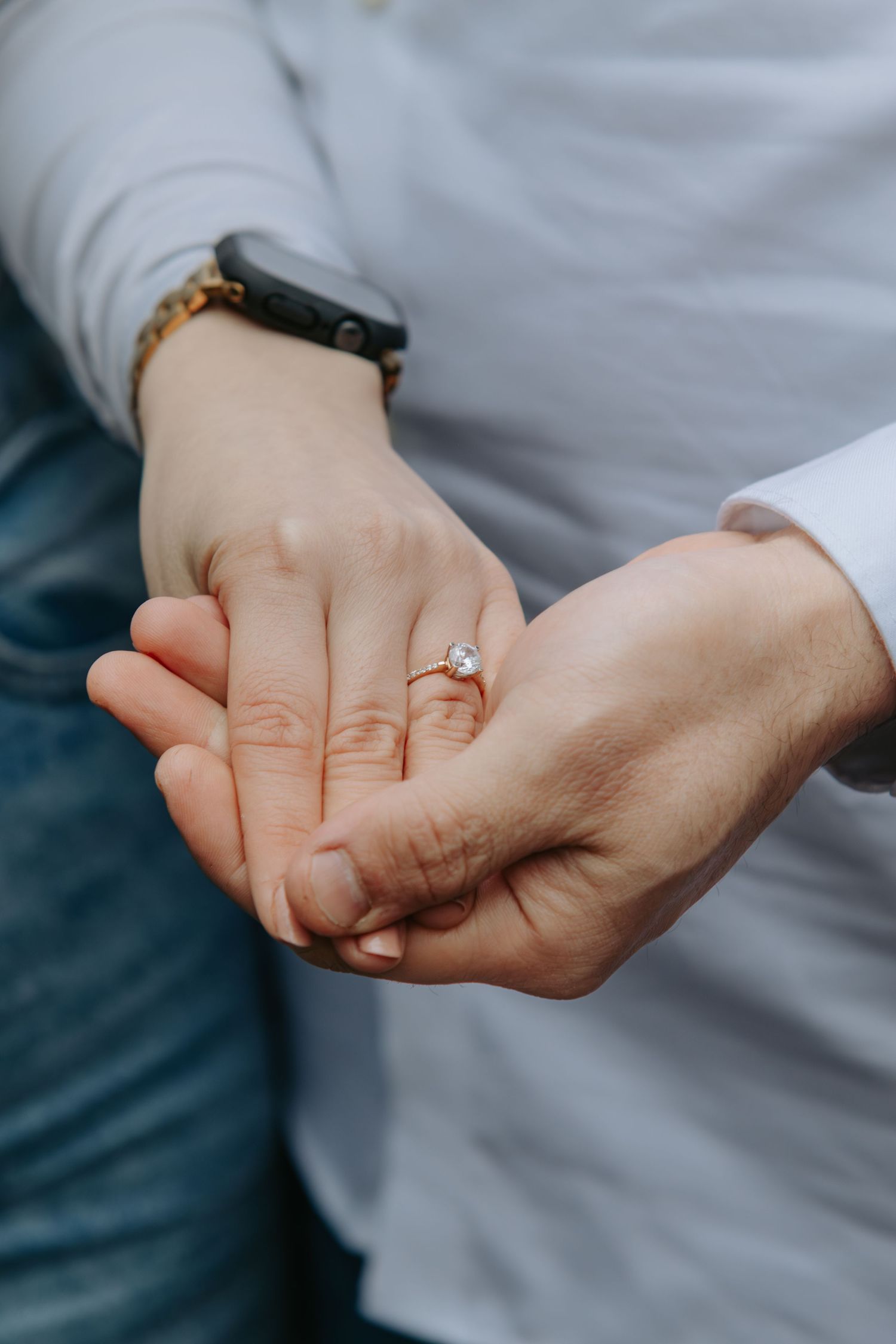 Close-up of couple holding hands with elegant diamond engagement ring and gold bracelet.